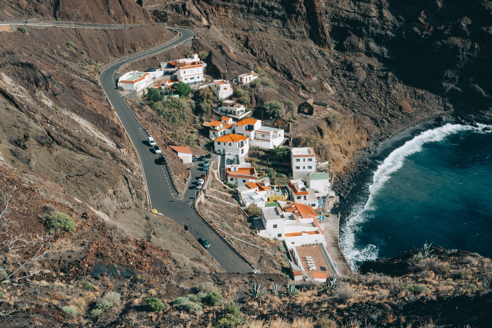 Pastel-colored houses perched precariously on steep volcanic cliff ledges overlooking the Atlantic Ocean
