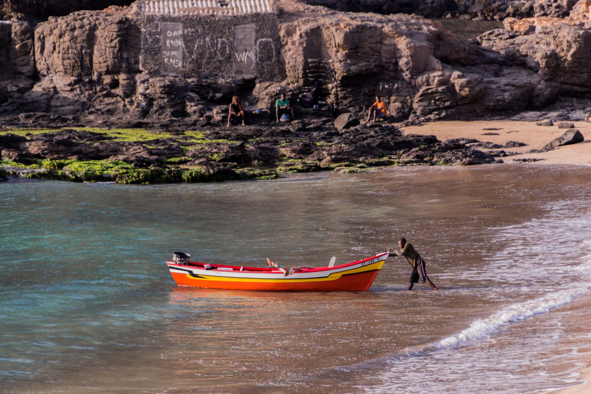 A local fisherman guiding a wooden boat through gentle coastal surf along a sandy beach
