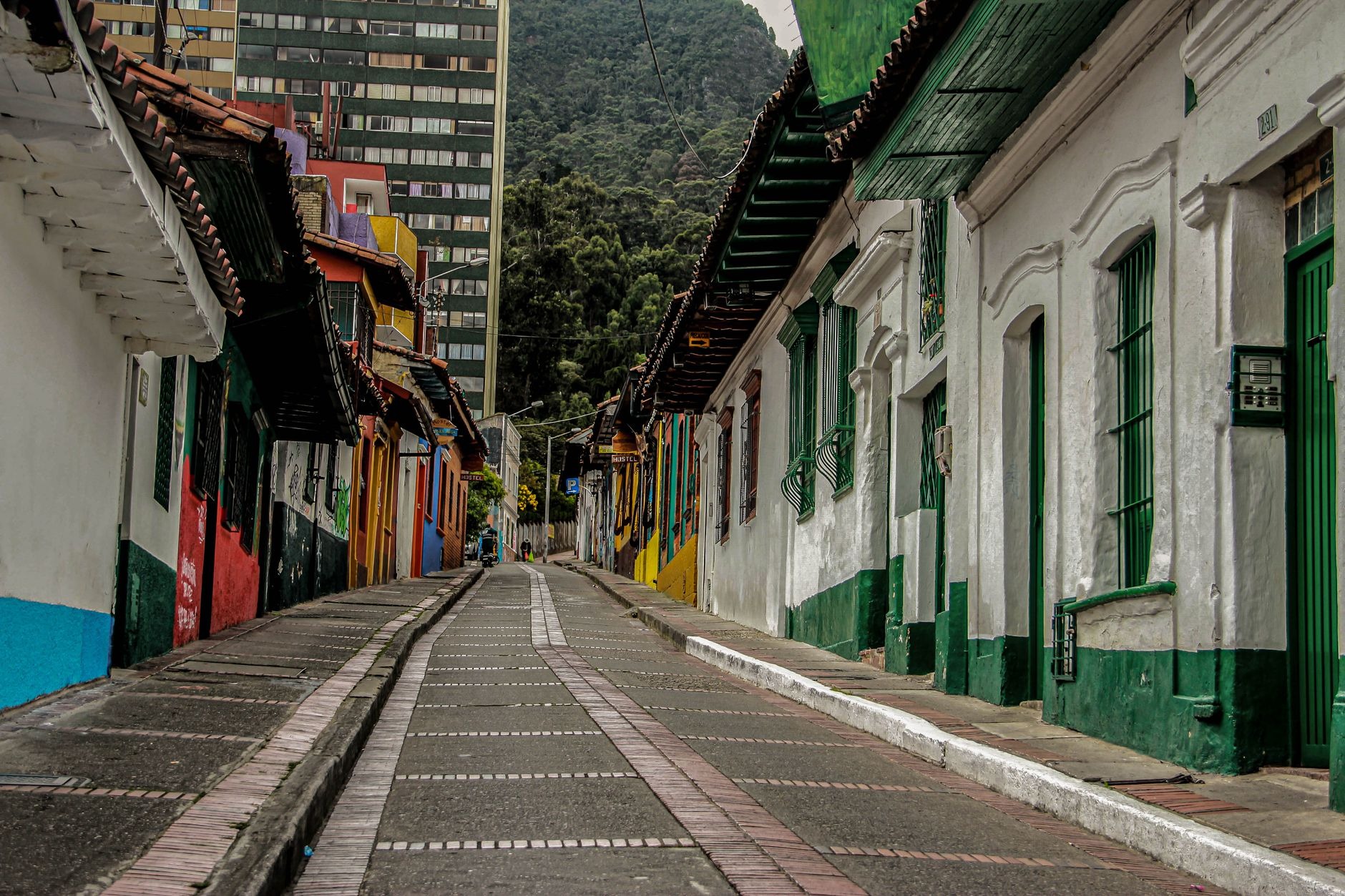 Steep cobblestone street framed by colorful Spanish colonial facades with the Monserrate mountain ridge rising behind La Candelaria in Bogotá