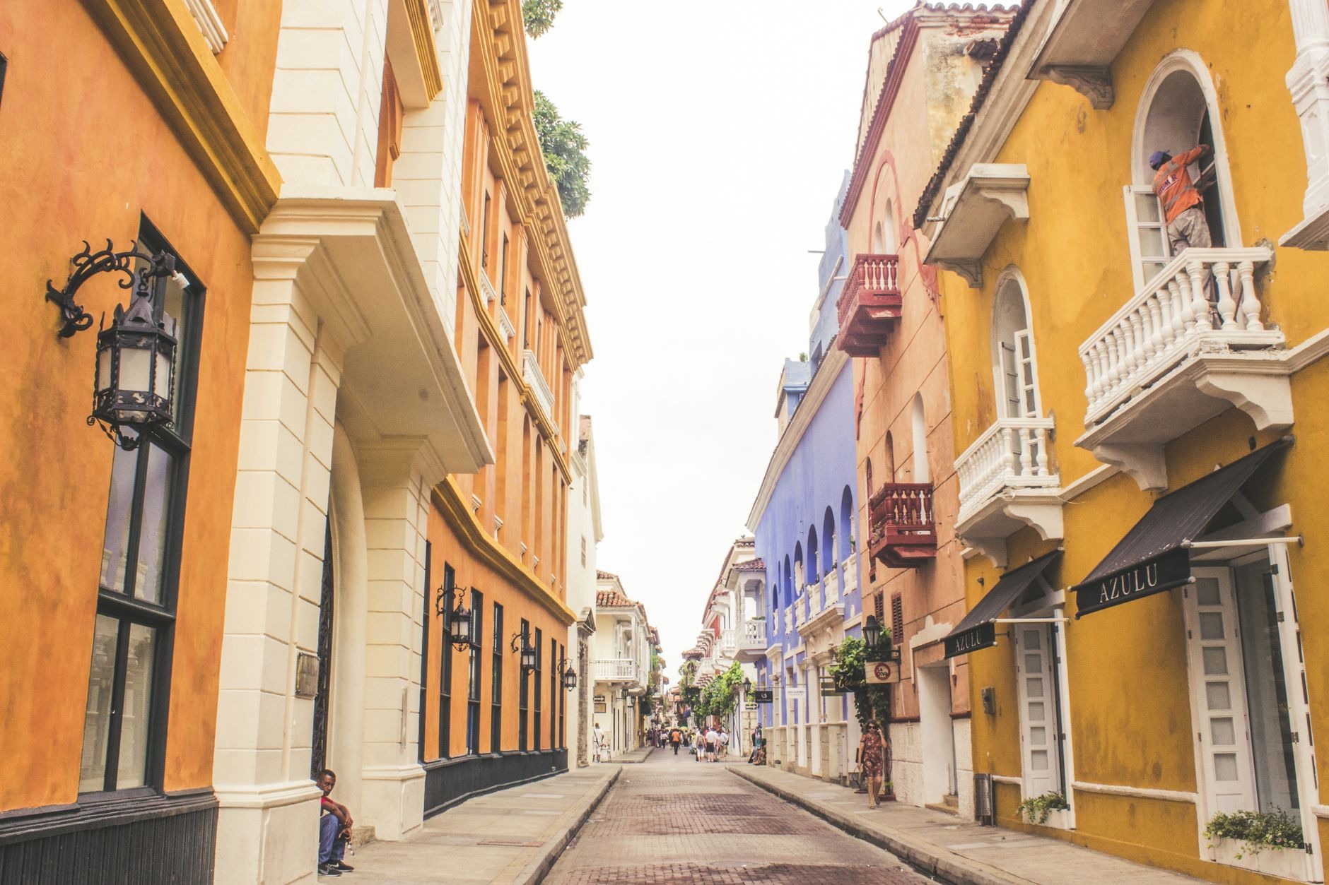 Sunlit colonial street in Cartagena's walled city lined with ornate wooden balconies overflowing with vibrant fuchsia bougainvillea flowers