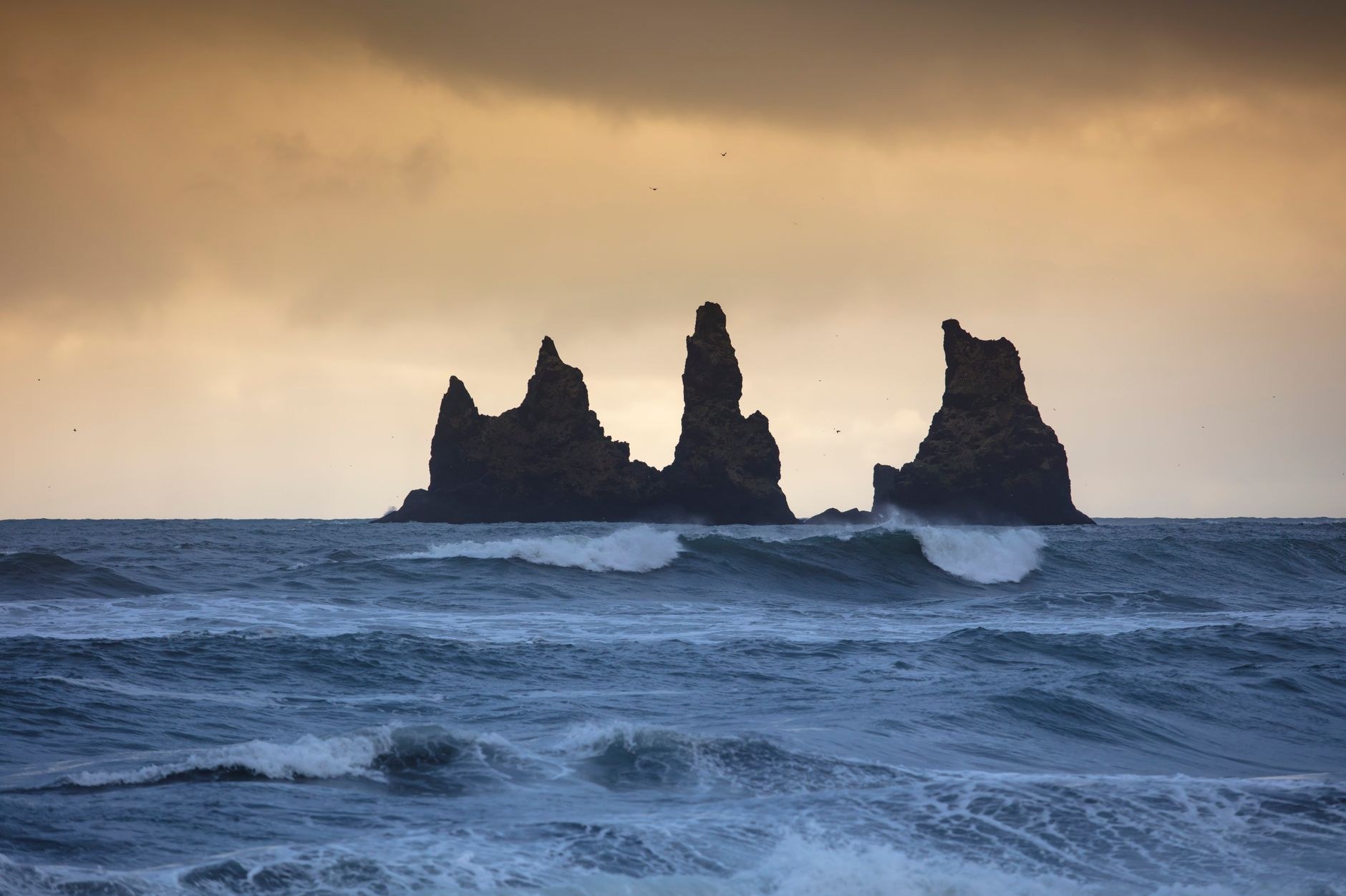 Surfers riding breaking Pacific waves past the iconic sea stack rock formation at sunset in El Tunco