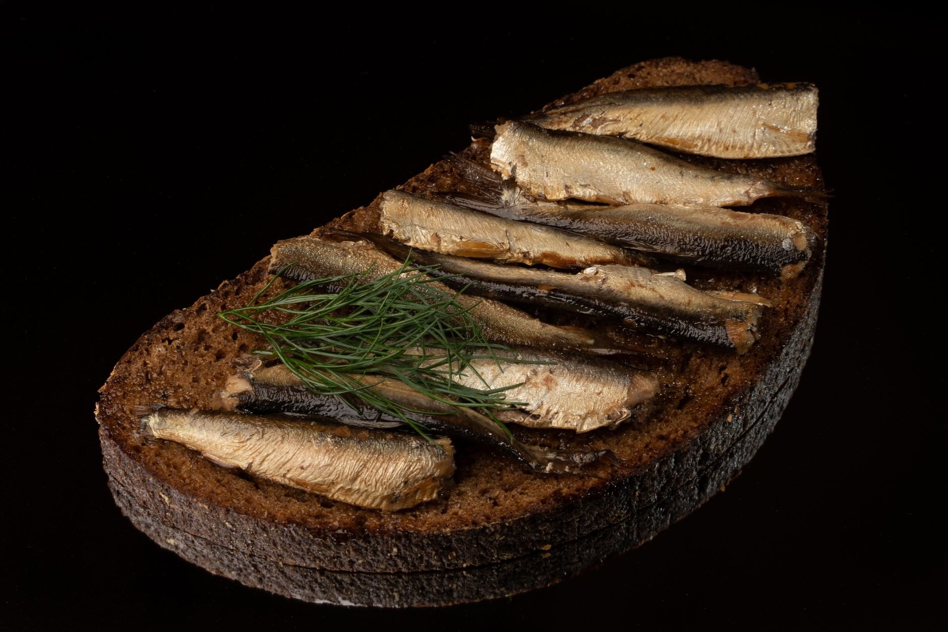 Artisan dark sourdough rye bread topped with spiced Baltic sprats, boiled egg slices, and fresh green dill