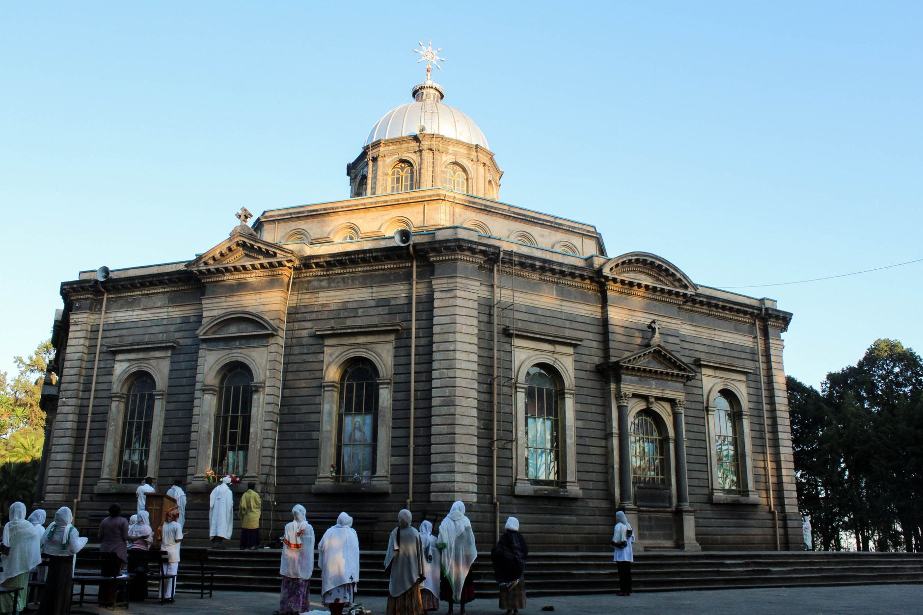 Orthodox worshippers draped in white cotton netela shawls gathering outside the stone facade of a historic cathedral