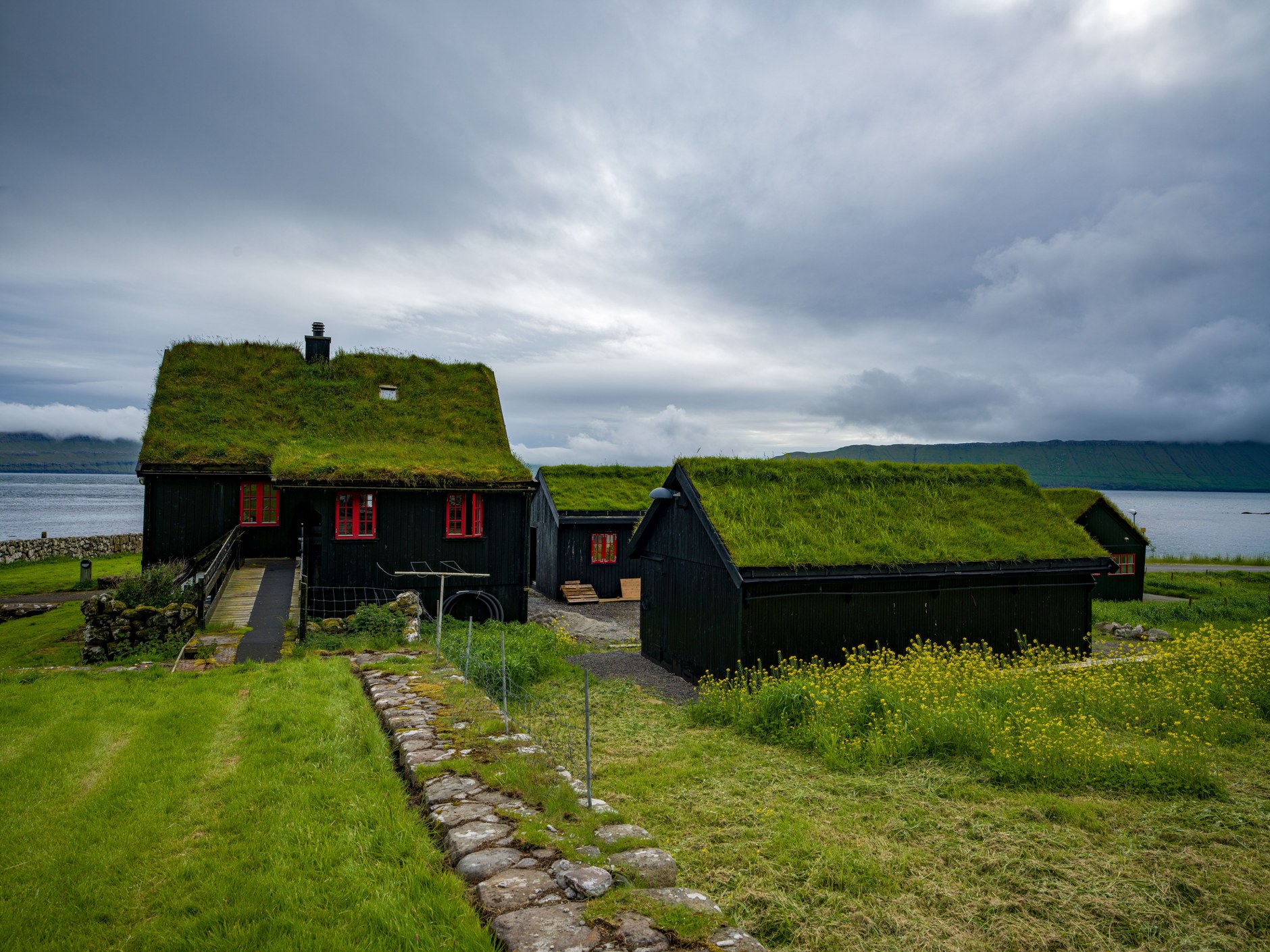 Quiet fjord waters bordered by green coastal slopes and grass-roofed outbuildings