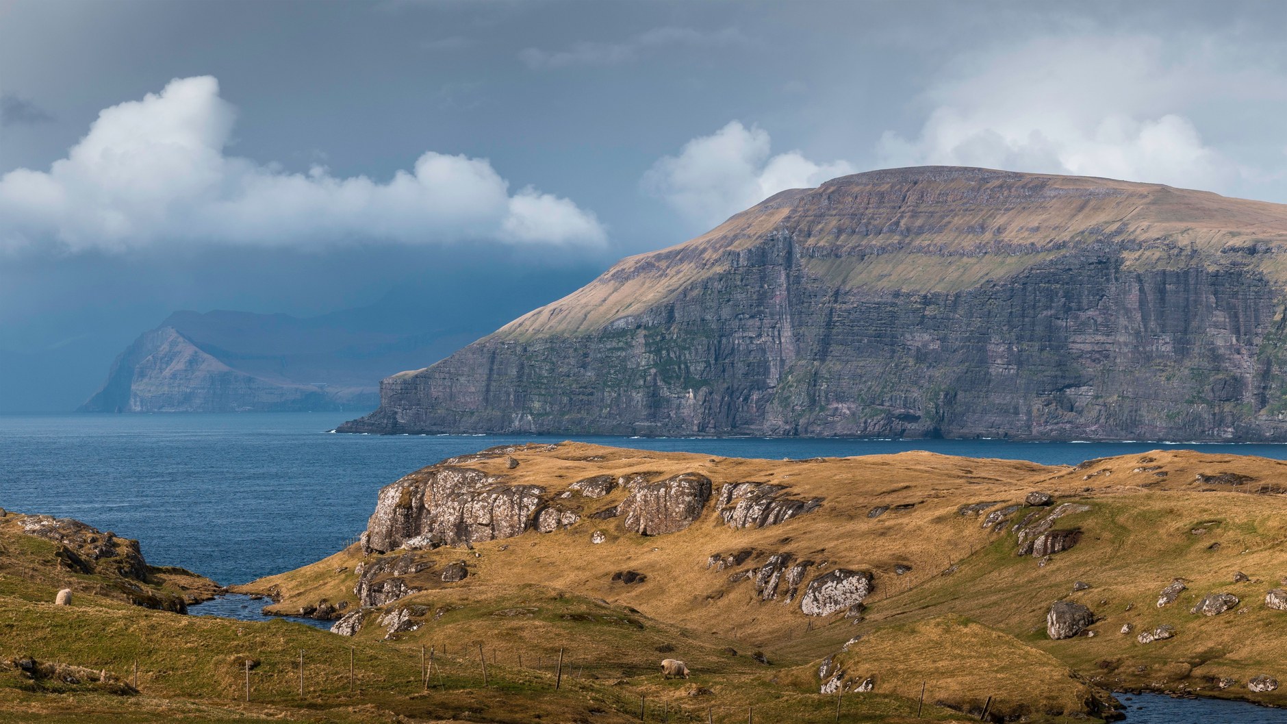 Layered basalt cliff headlands and deep oceanic sounds under moody North Atlantic skies