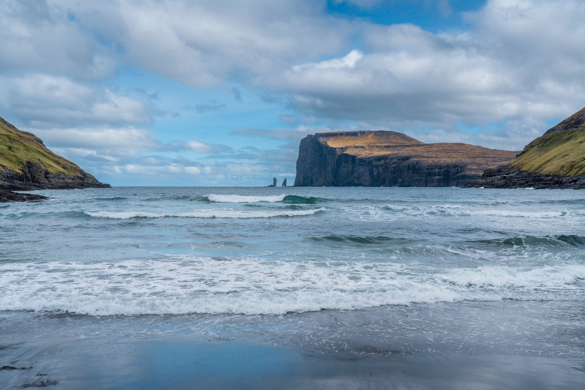 Sweeping coastal fjord bay with black volcanic sand beach framed by towering green mountain peaks