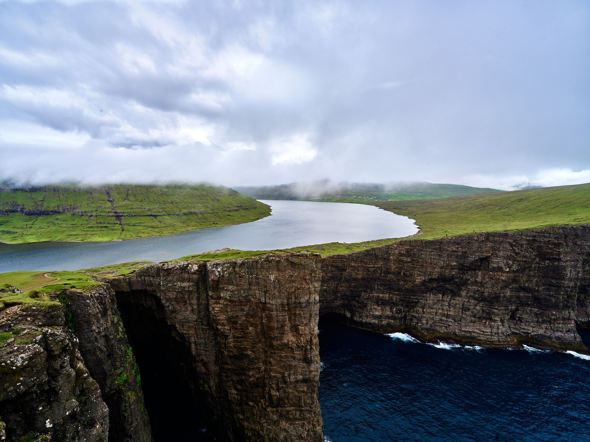 High basalt sea cliffs rising above the Atlantic Ocean beside the perched waters of Lake Sorvagsvatn