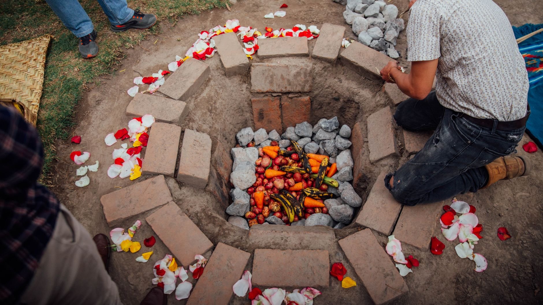 Banana-leaf wrapped parcels of pork, chicken, and dalo root being lifted from a traditional Fijian lovo underground hot stone earth oven