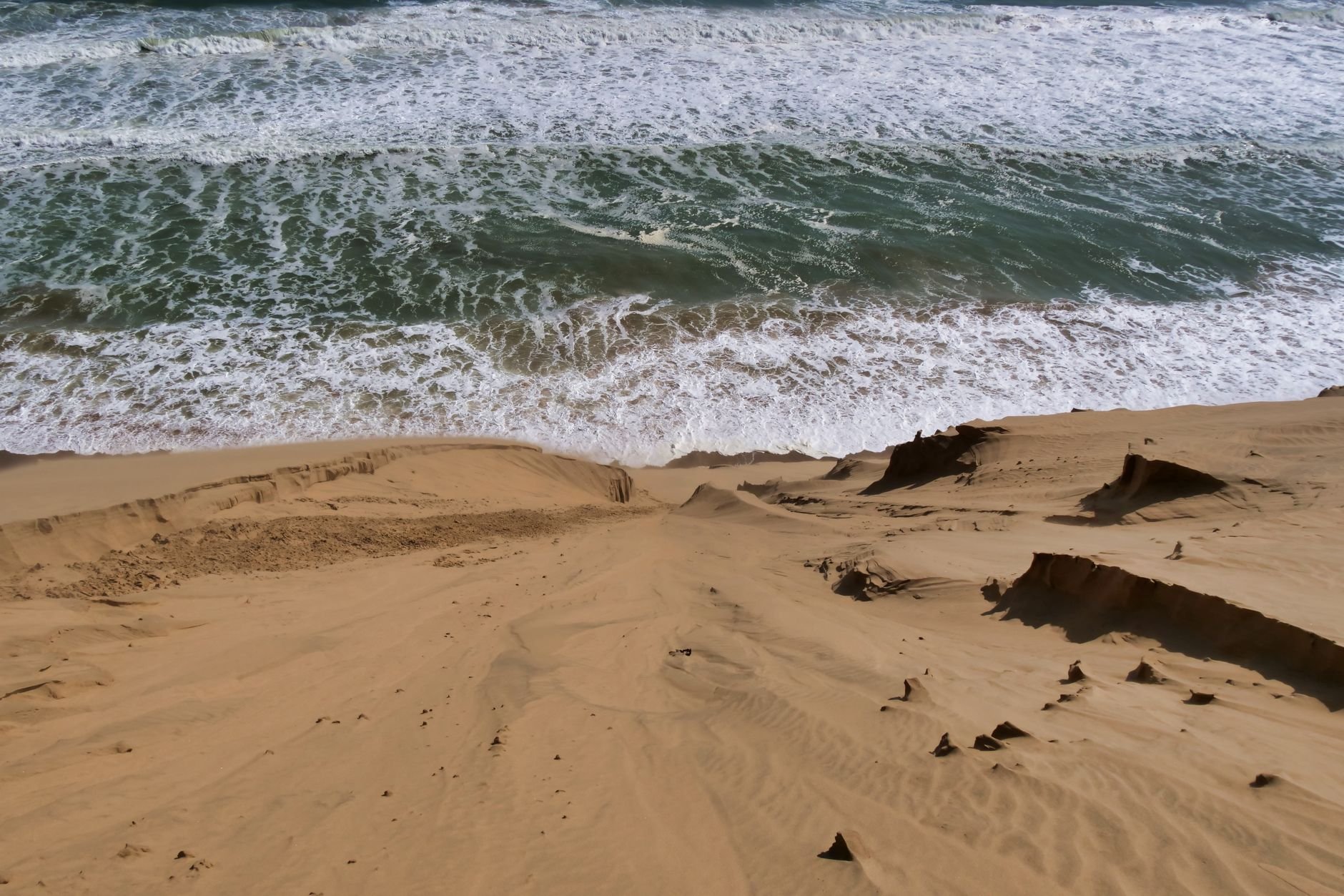 Sweeping parabolic coastal sand dunes covered in hardy maritime grass meeting crashing Pacific ocean surf at Sigatoka