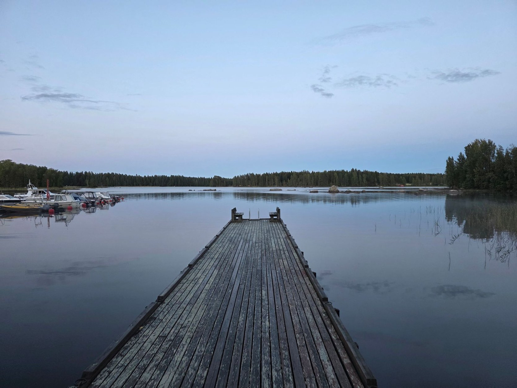 Rustic wooden sauna cabin and timber swimming dock extending into a tranquil Finnish lake surrounded by pine forests