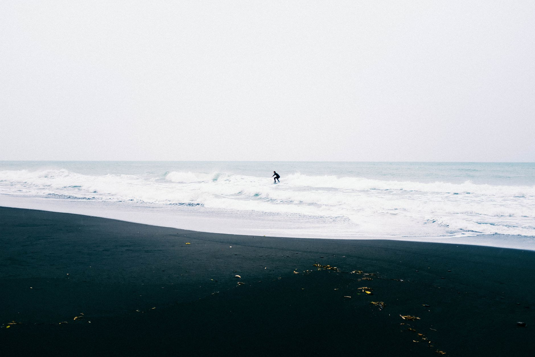 Surfer paddling out past breaking ocean swell along a volcanic black sand coastline in Tahiti