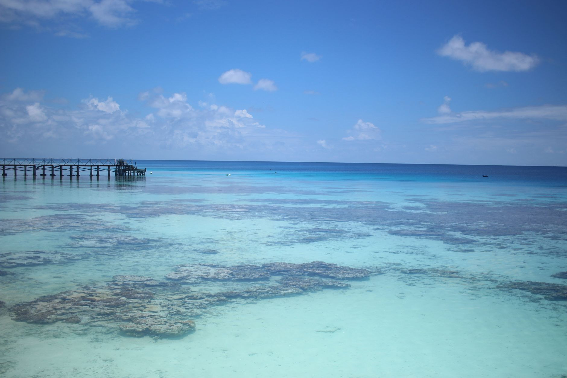 Wooden jetty stretching into the endless calm sapphire waters of a vast coral atoll in the Tuamotus