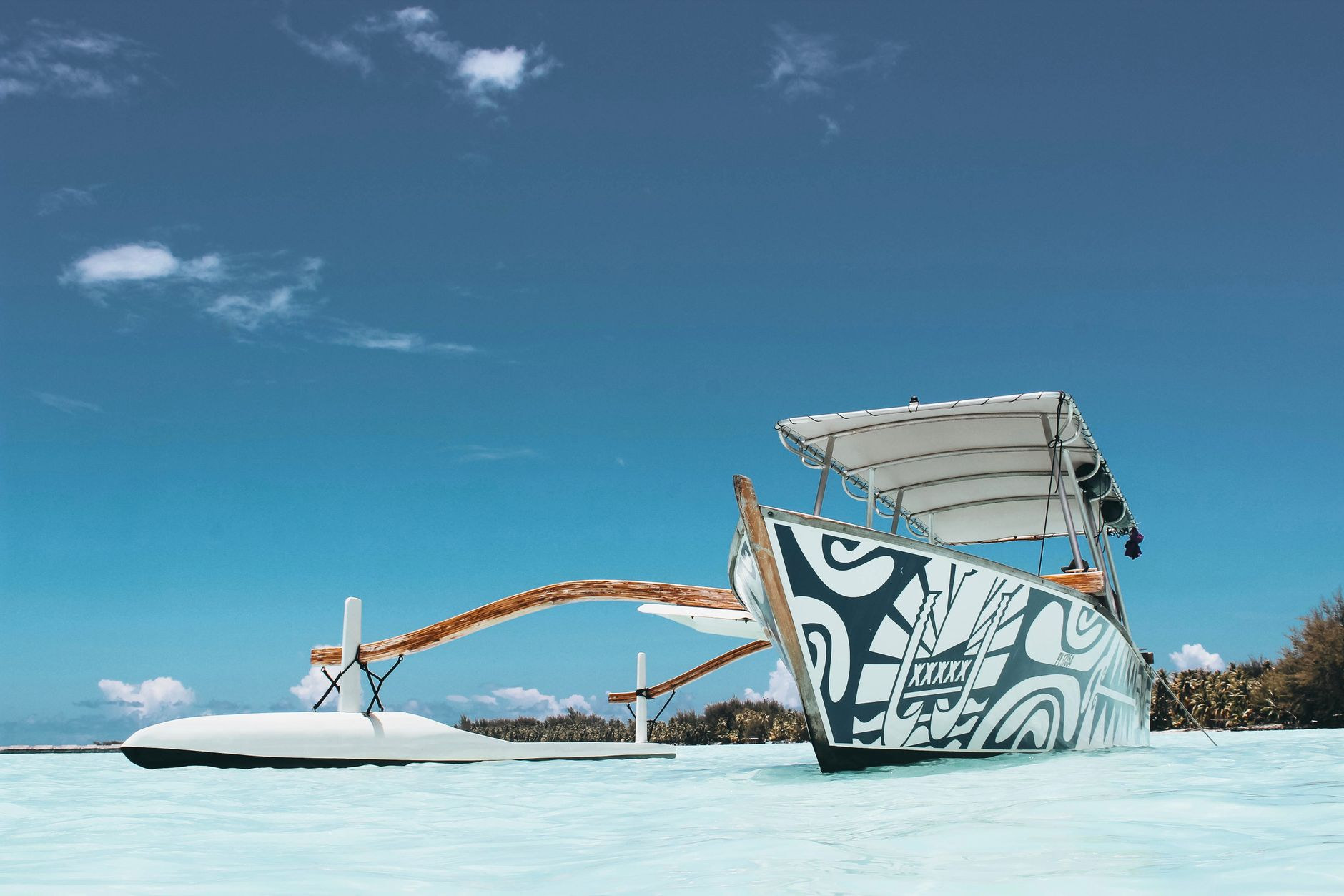 Traditional Polynesian outrigger canoe floating on translucent turquoise lagoon waters near Vaitape