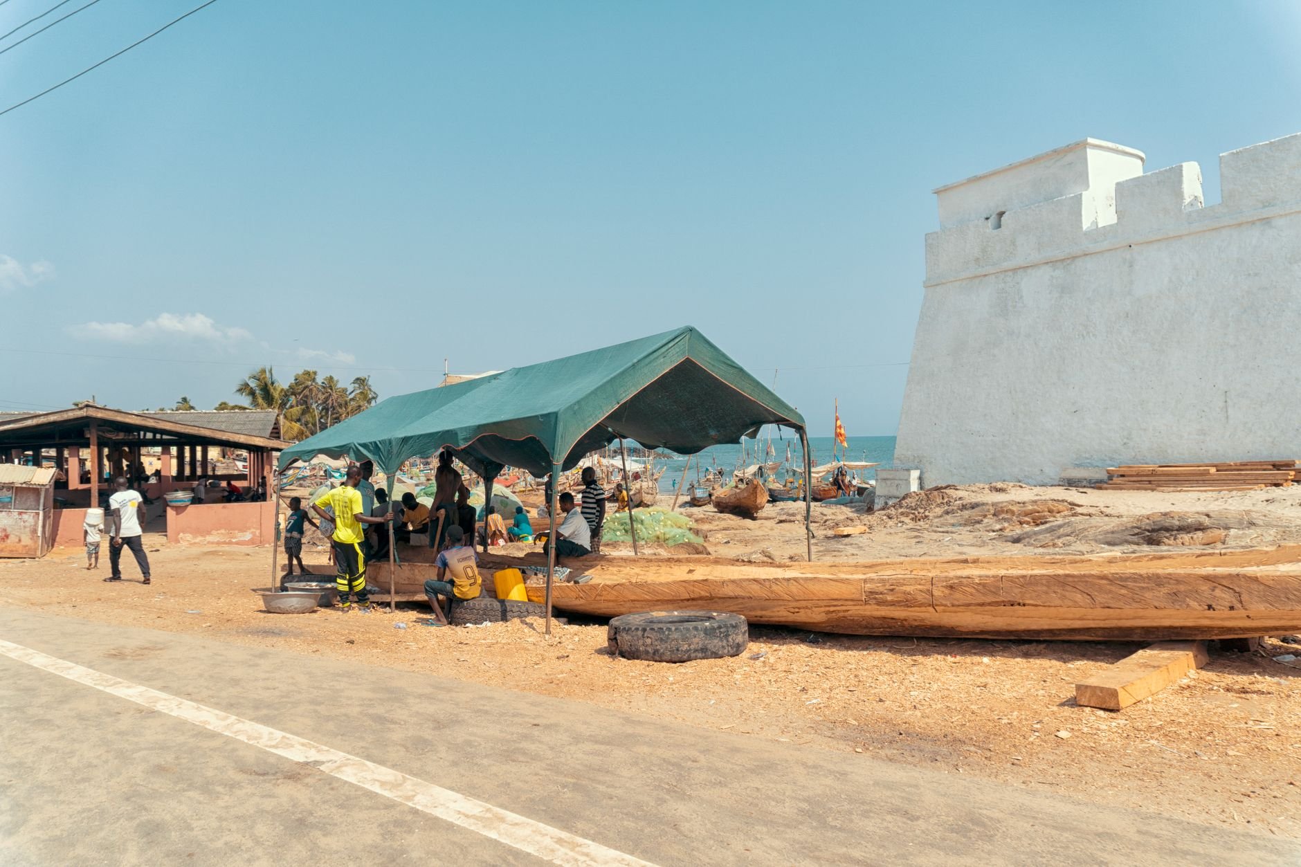 Extensive stone battlements and towers of Elmina Castle rising above a bustling fishing harbor packed with colorful wooden pirogues