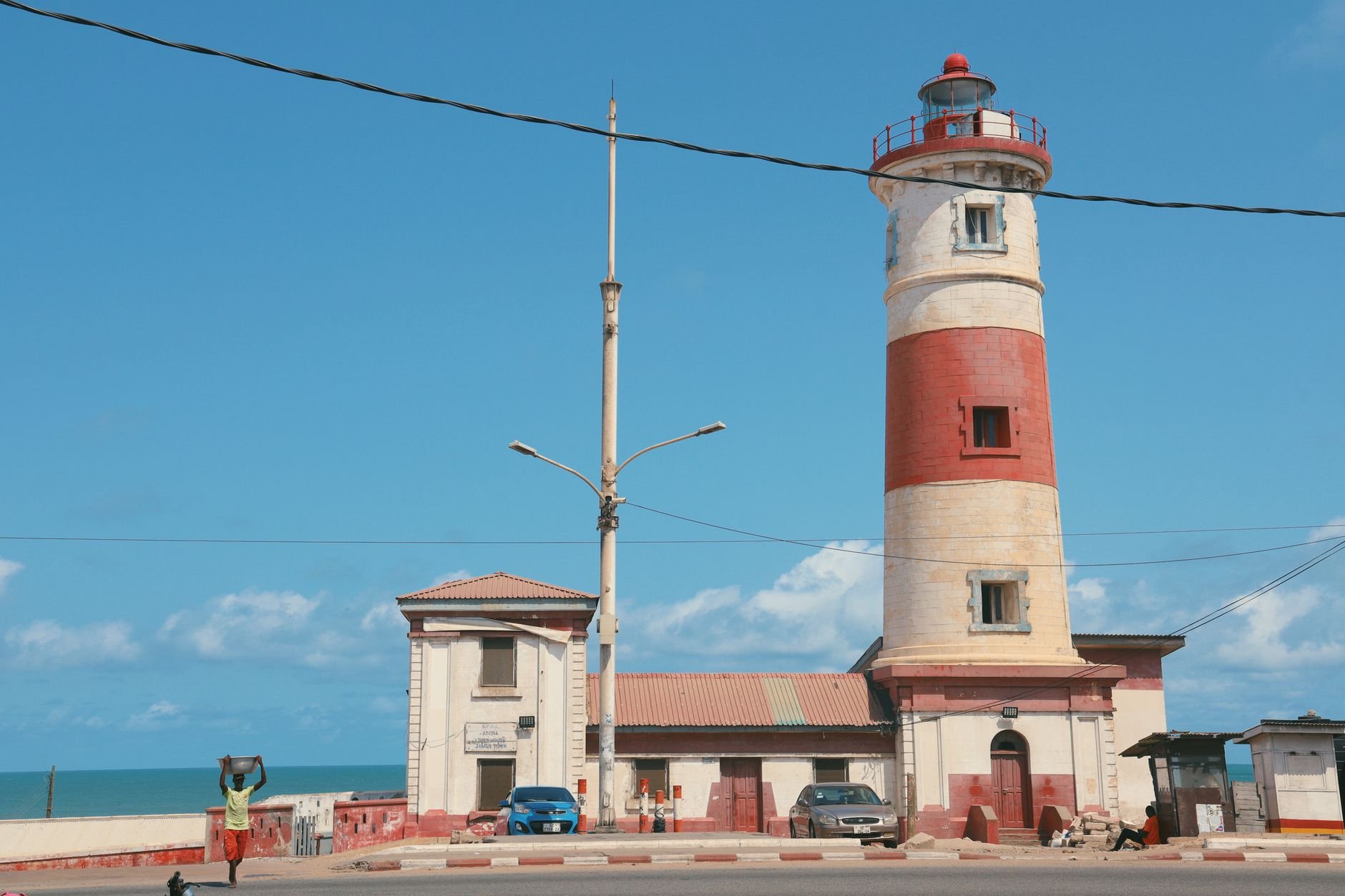 Red and white striped colonial lighthouse tower rising above the historic fishing harbor and wooden canoes of Jamestown in coastal Accra