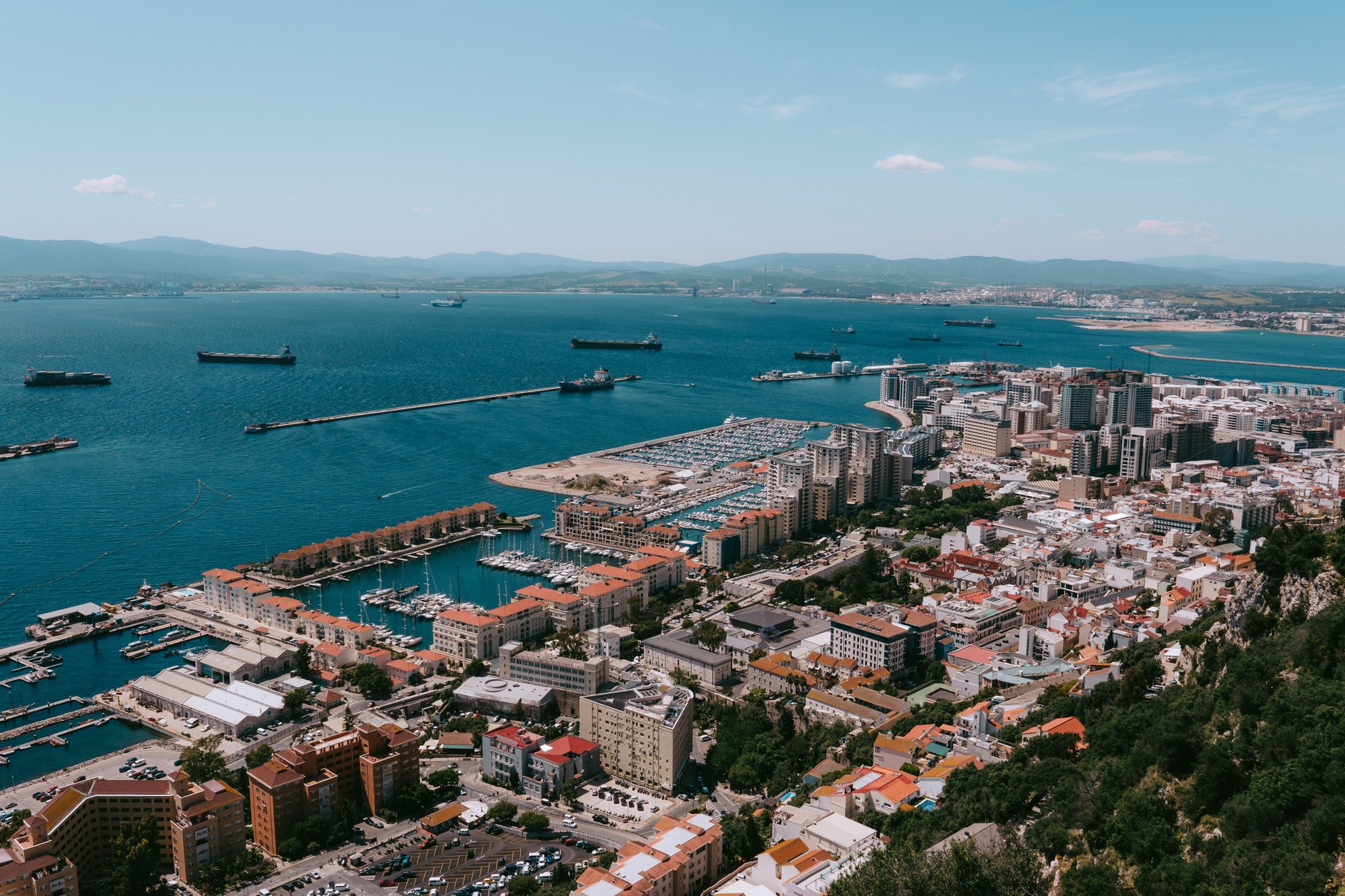 Aerial view of Gibraltar harbor with commercial shipping docks, marina berths, and dense town below the cliffs