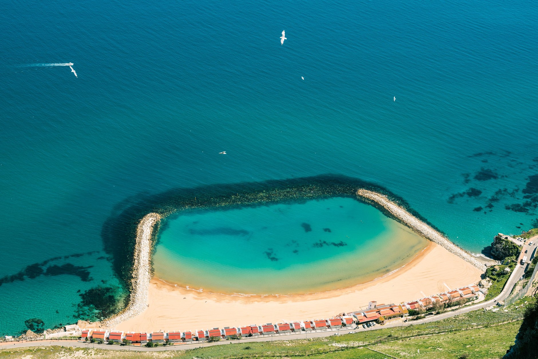 Aerial view of a sandy beach cove protected by stone groynes beneath towering limestone cliffs in Gibraltar