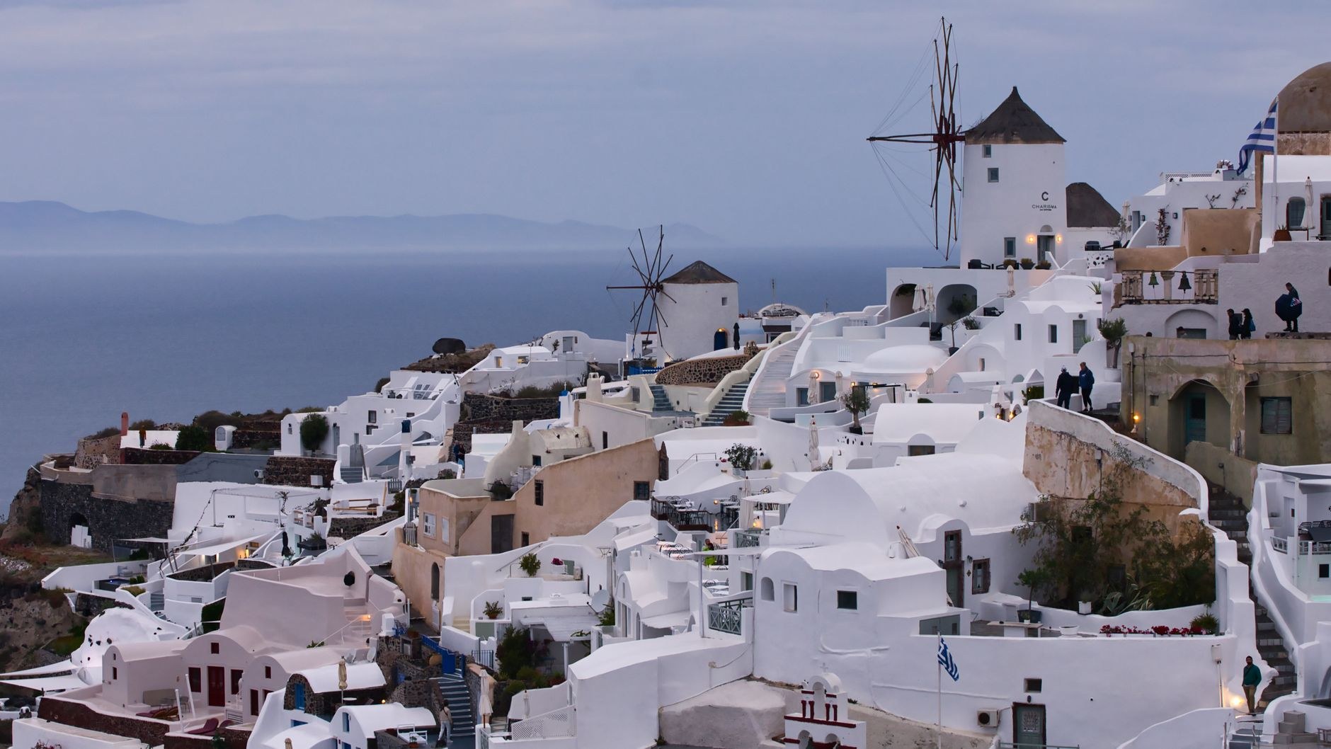 Tiered whitewashed cliffside dwellings and windmill bathed in golden sunset light in Oia