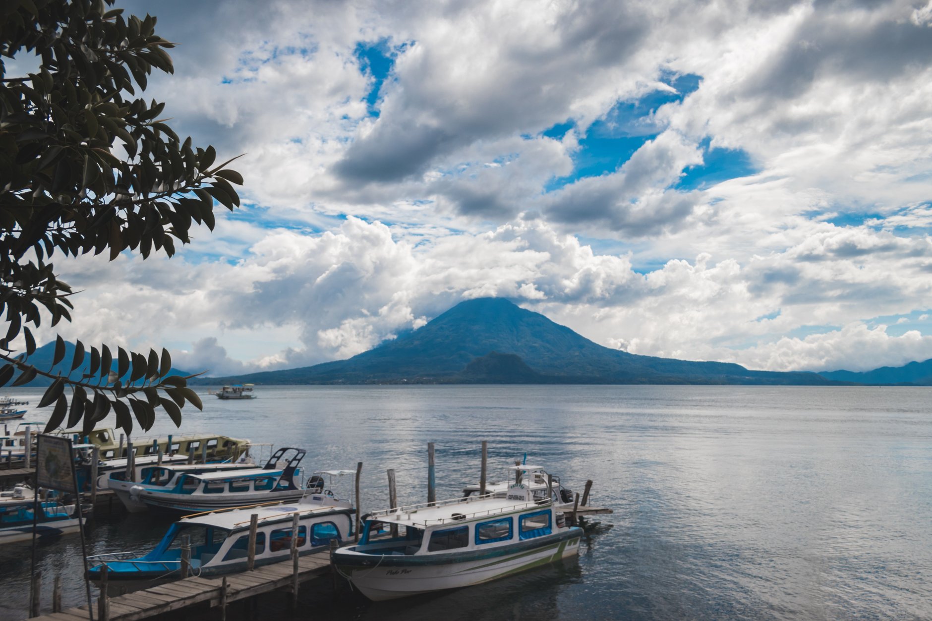 Wooden boat jetty on Lake Atitlan with passenger lancha boats moored against a background of conical volcanic peaks
