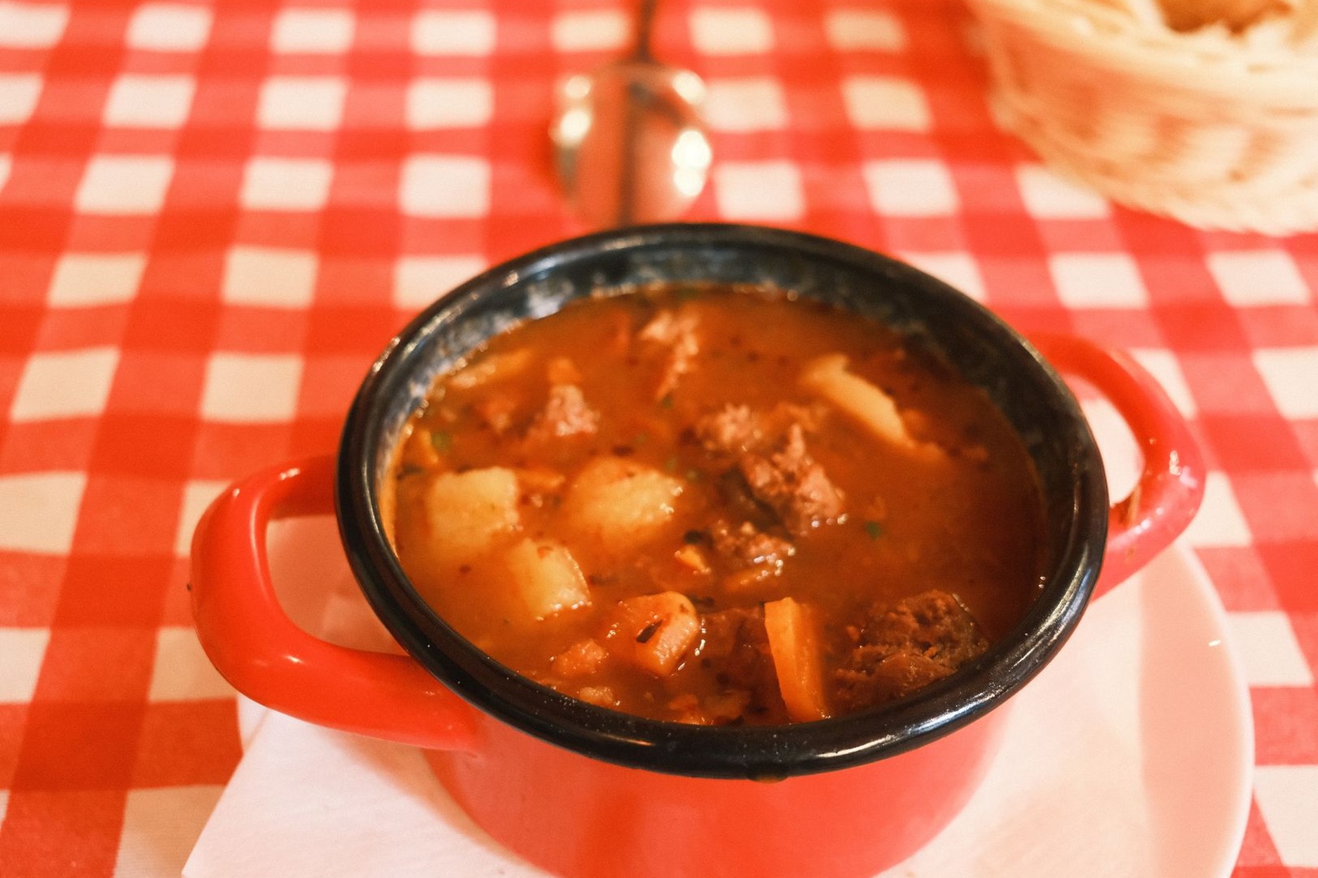 Traditional Hungarian beef goulash soup served in a red enameled pot with fresh crusty bread and sliced chili peppers