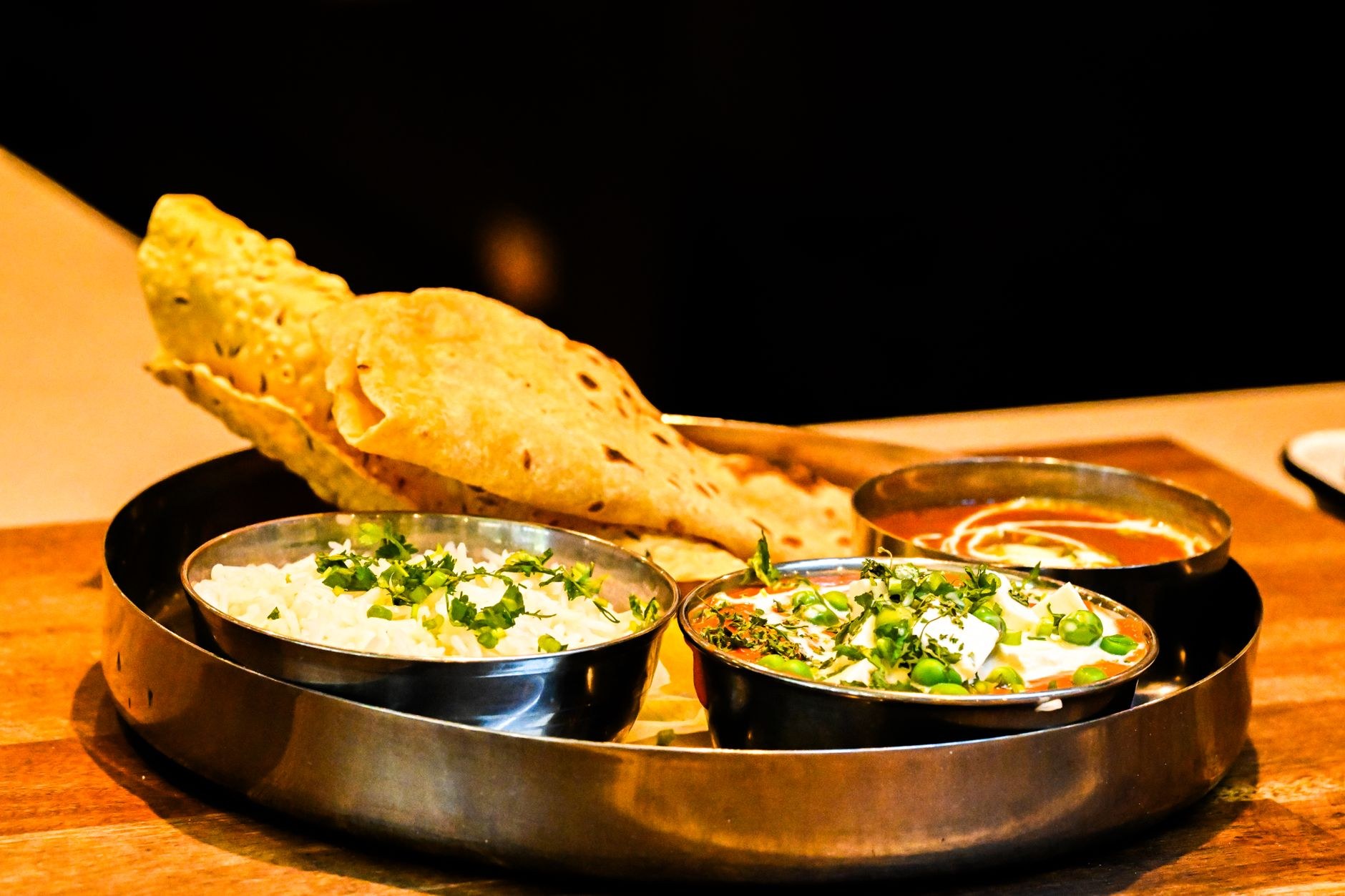 Traditional brass thali platter with bowls of dal, paneer, aromatic basmati rice, and fresh tandoori roti