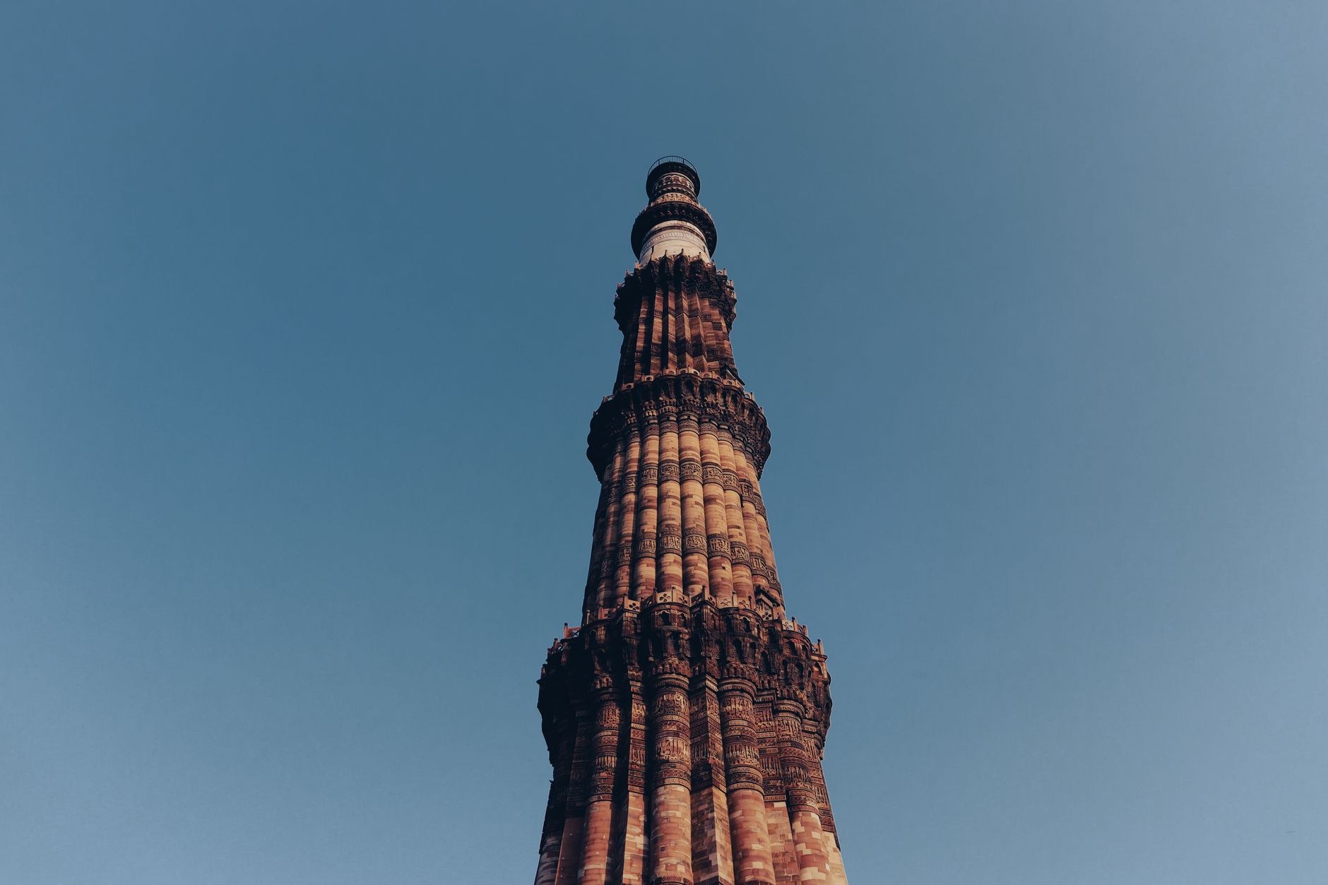 Towering 73-meter fluted red sandstone minaret of Qutub Minar soaring into a blue sky