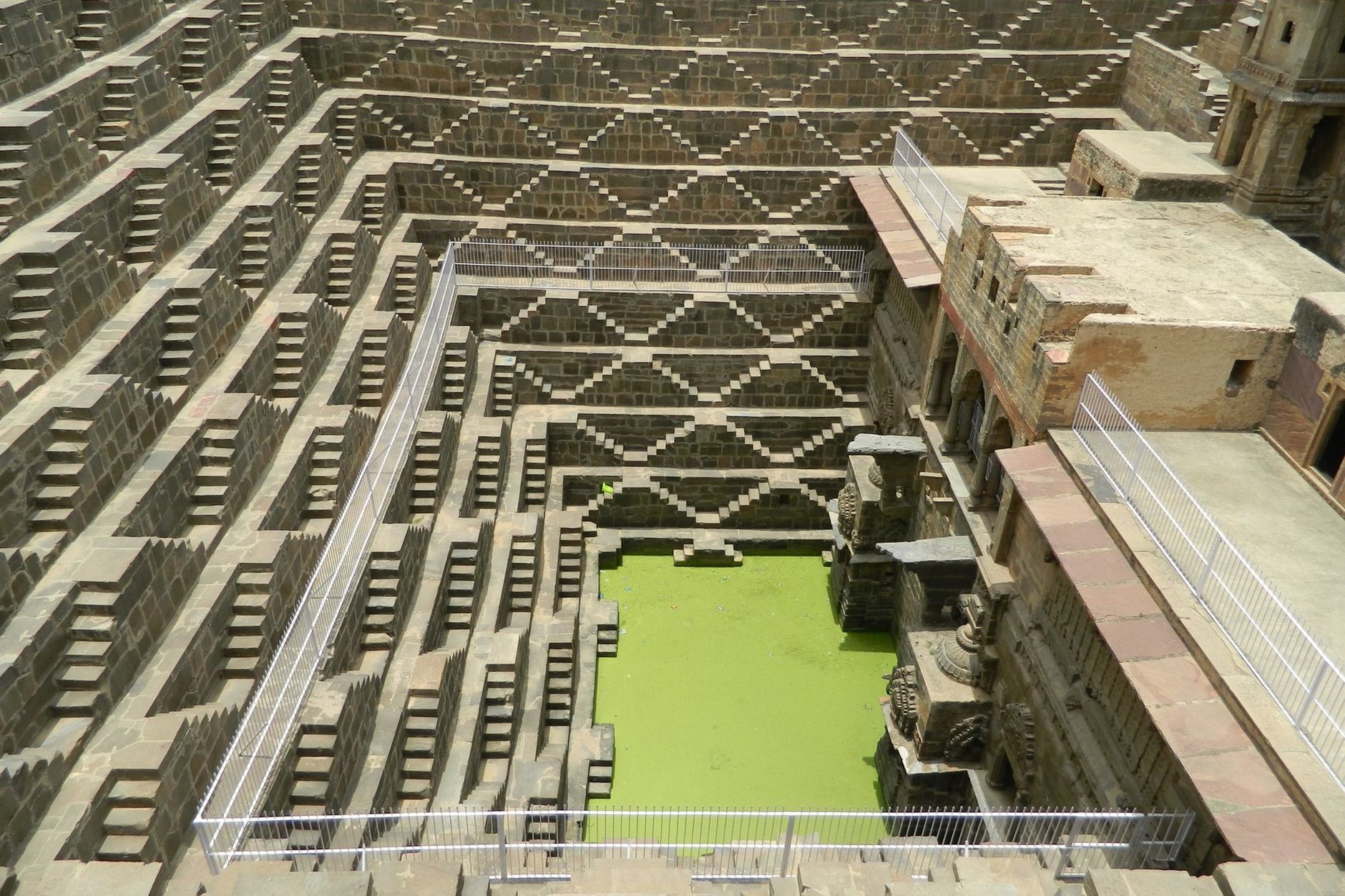 Massive ancient geometric stone stepwell with thousands of symmetrical staircases descending into green water