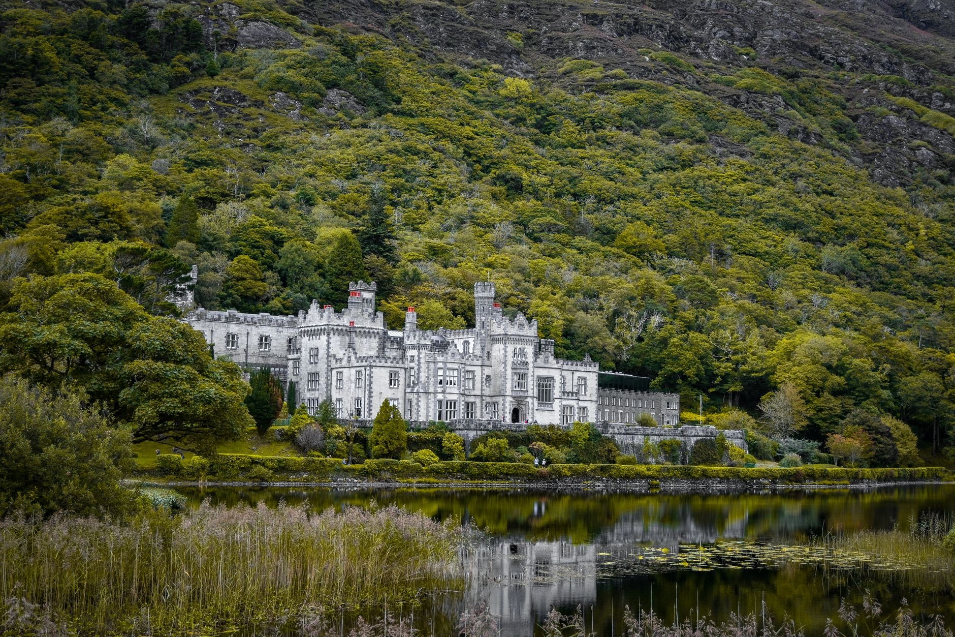 Neogothic stone facade of Kylemore Abbey reflecting on the tranquil waters of Pollacappall Lough in Connemara