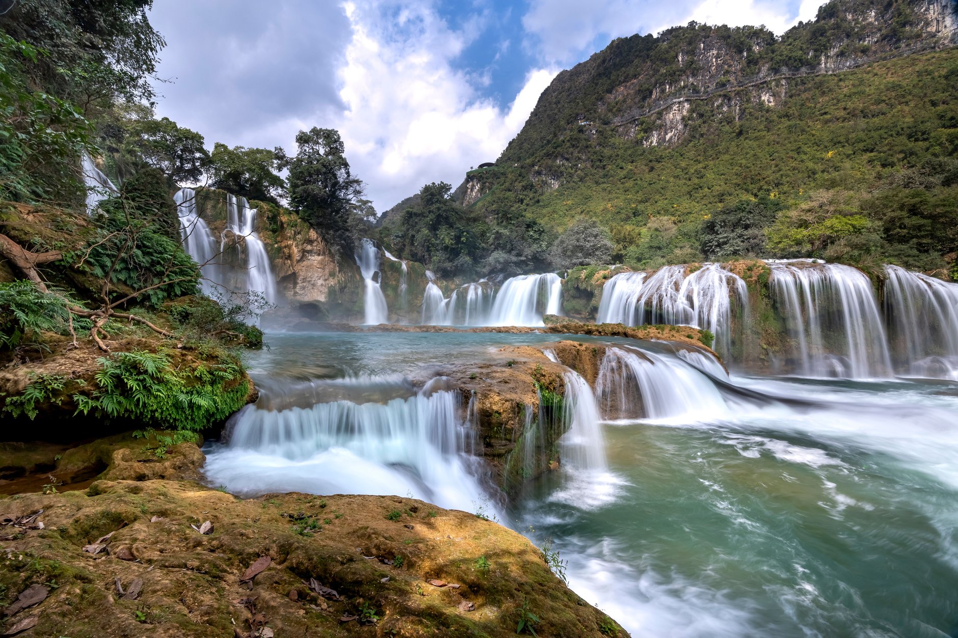 Natural limestone tiered waterfall flowing down through tropical trees directly onto a golden Caribbean sand beach