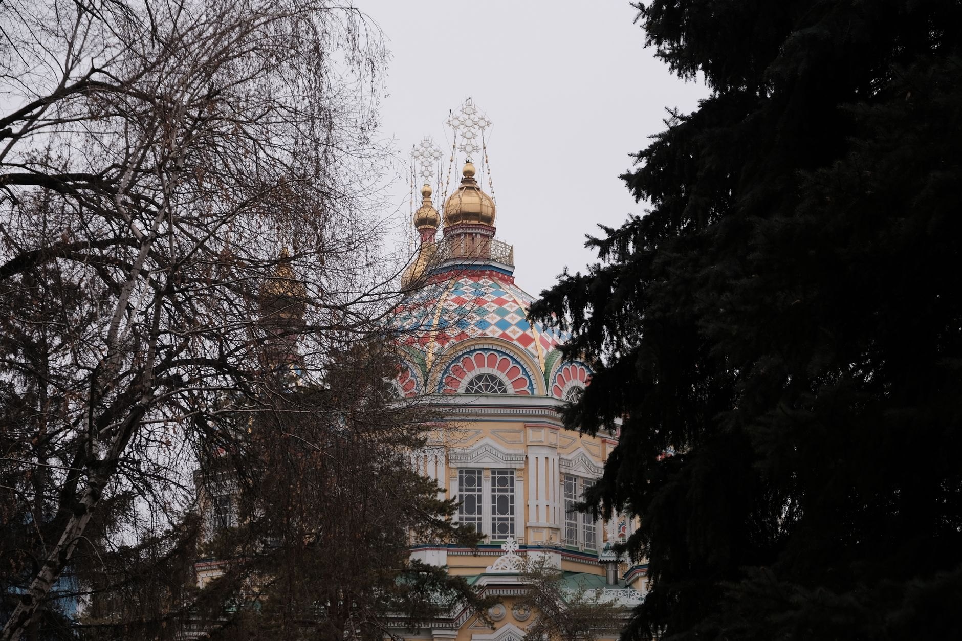 Pastel yellow wooden Ascension Cathedral with colorful onion domes and gold crosses in Panfilov Park