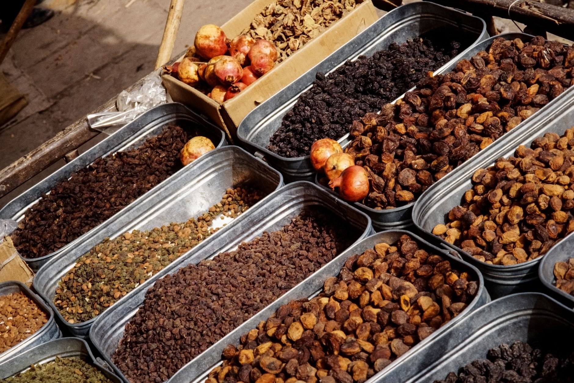 Abundant market stalls displaying mounds of dried apricots, walnuts, almonds, and colorful central Asian spices