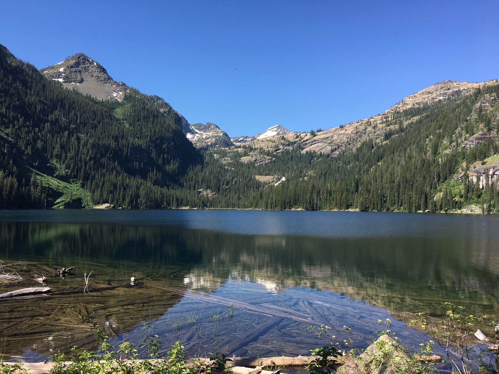 Deep blue alpine waters of Lower Kolsai Lake framed by steep slopes of Tian Shan spruce and snow-dusted peaks