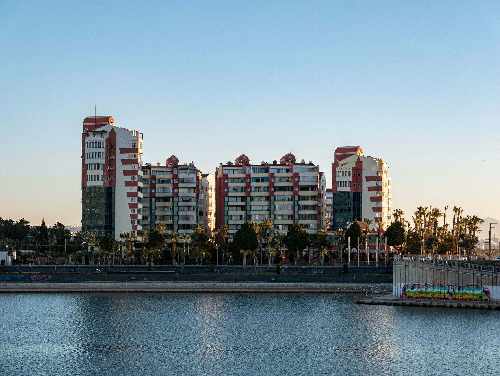 A landscaped waterfront promenade with palm trees and modern stone walkways bordering the calm sea