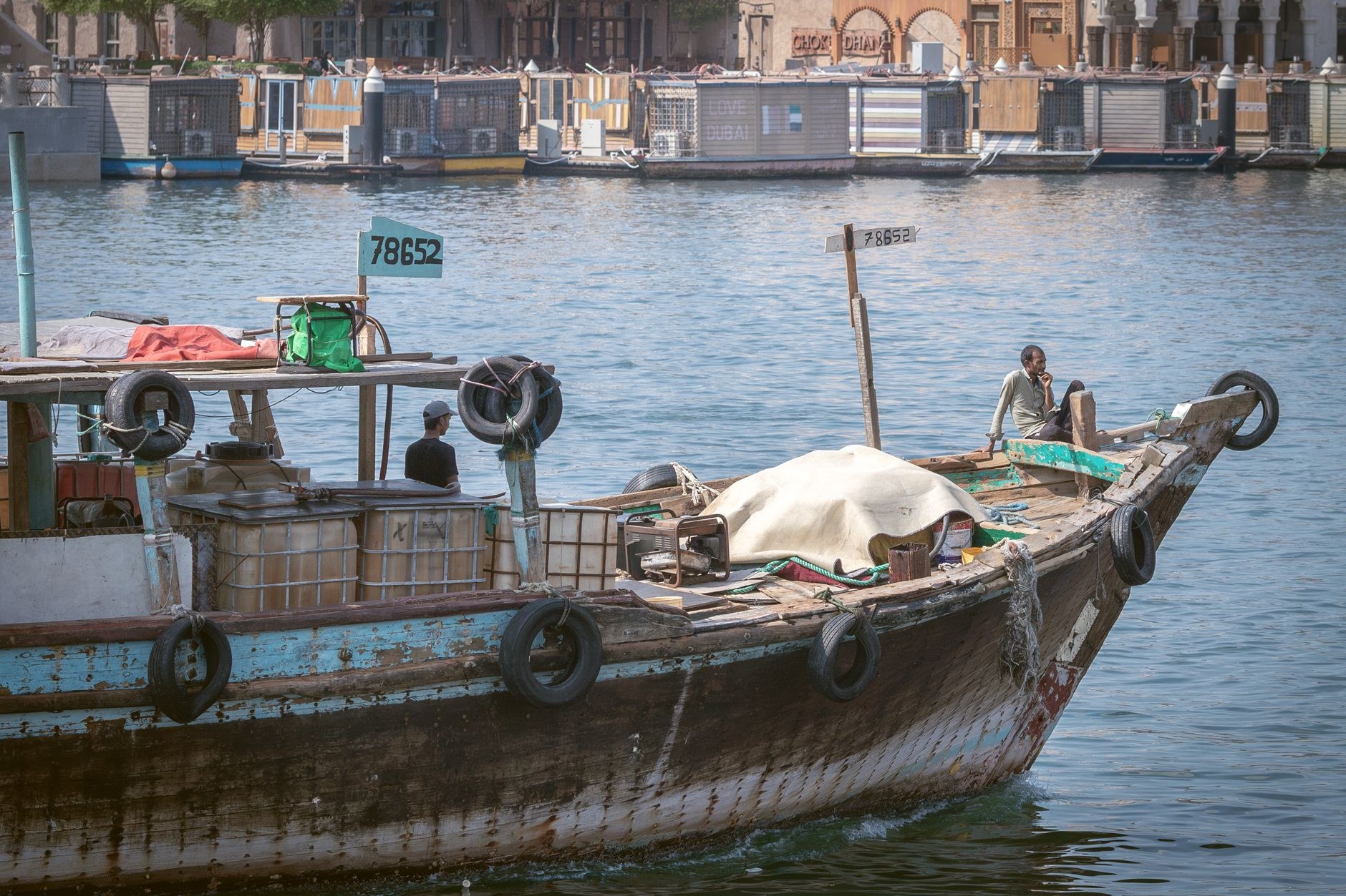 Traditional handcrafted wooden dhow boats moored along a stone quayside in turquoise harbor water