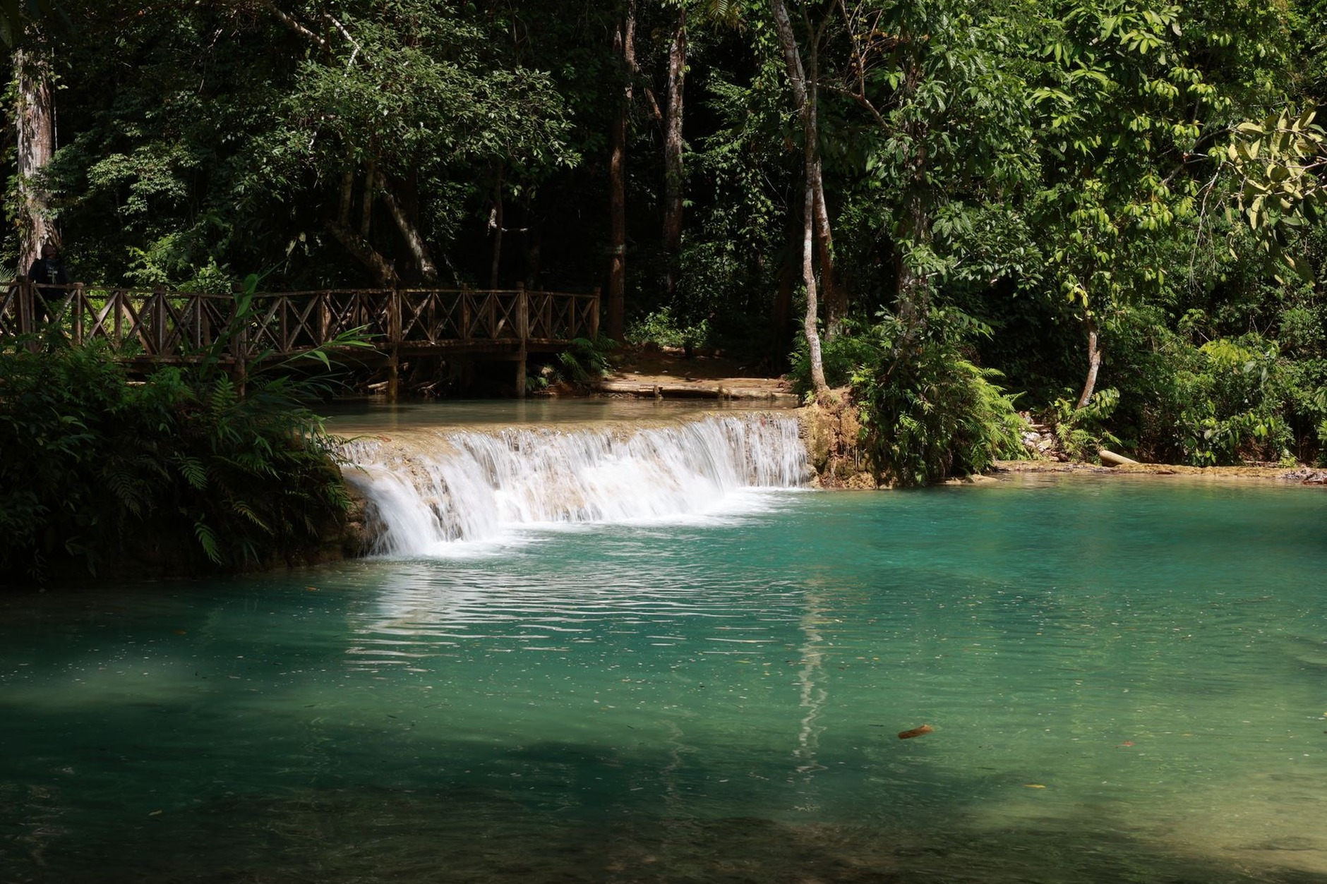Multi-tiered turquoise cascade tumbling into natural limestone swimming pools surrounded by lush green jungle at Kuang Si Falls