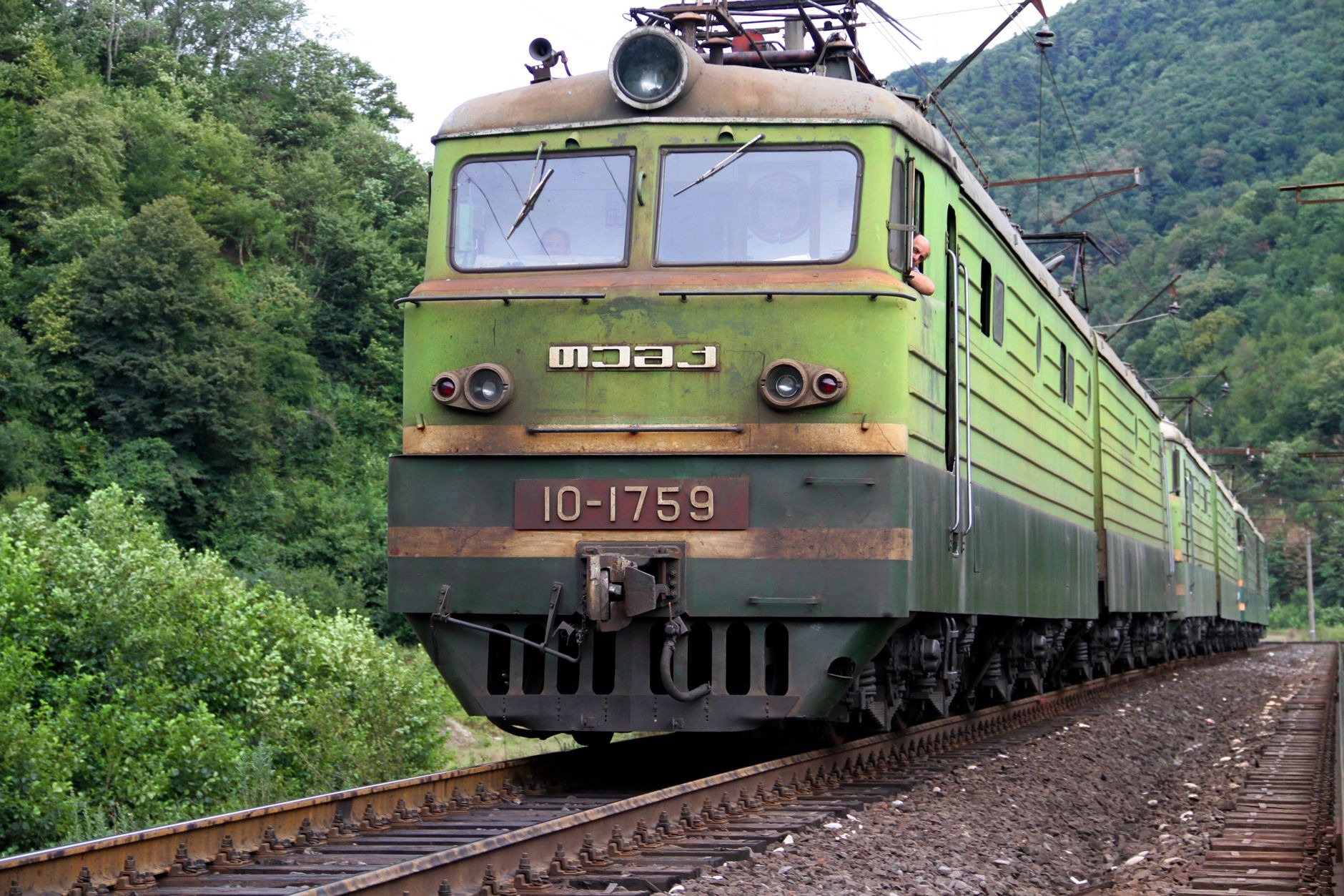 Modern passenger train traveling through a lush tropical mountain valley on elevated viaduct tracks