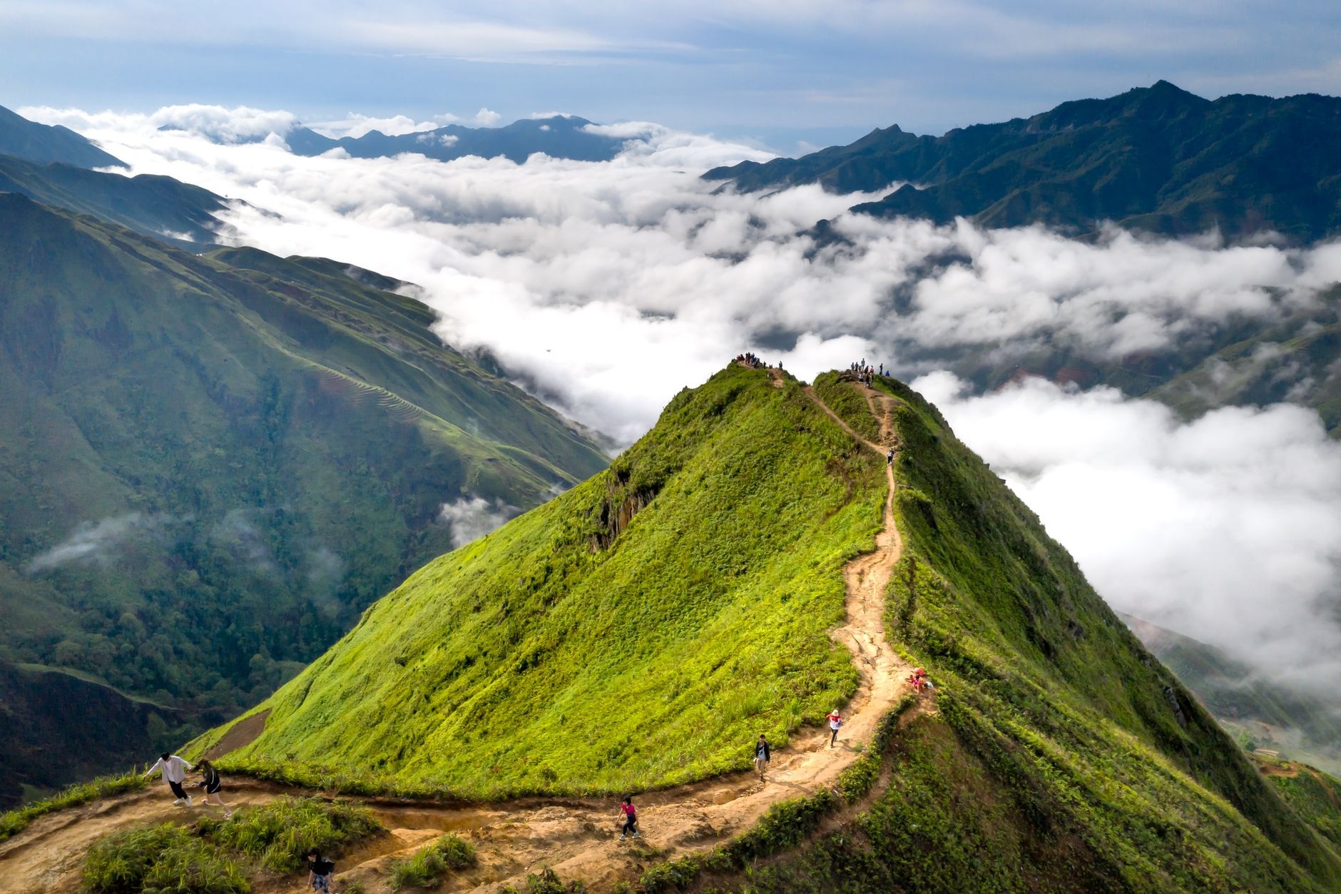 Panoramic summit view overlooking jagged karst mountain ridges and patchwork green rice fields from a high tropical viewpoint