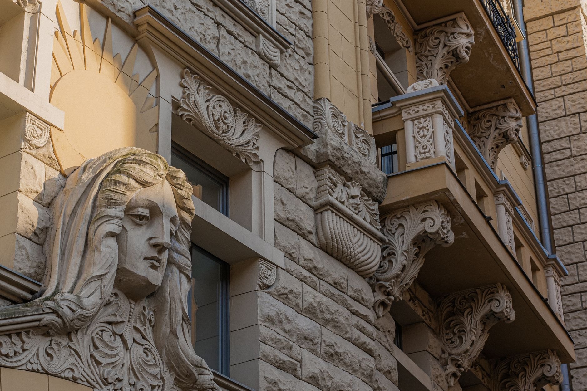 Intricate stone sculptures, gargoyles, and floral motifs carved into an Art Nouveau apartment facade on Alberta iela