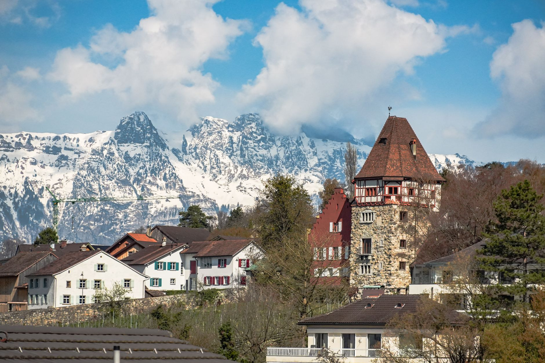 Peaceful village houses of Balzers framed against towering snow-dusted alpine limestone peaks under blue sky