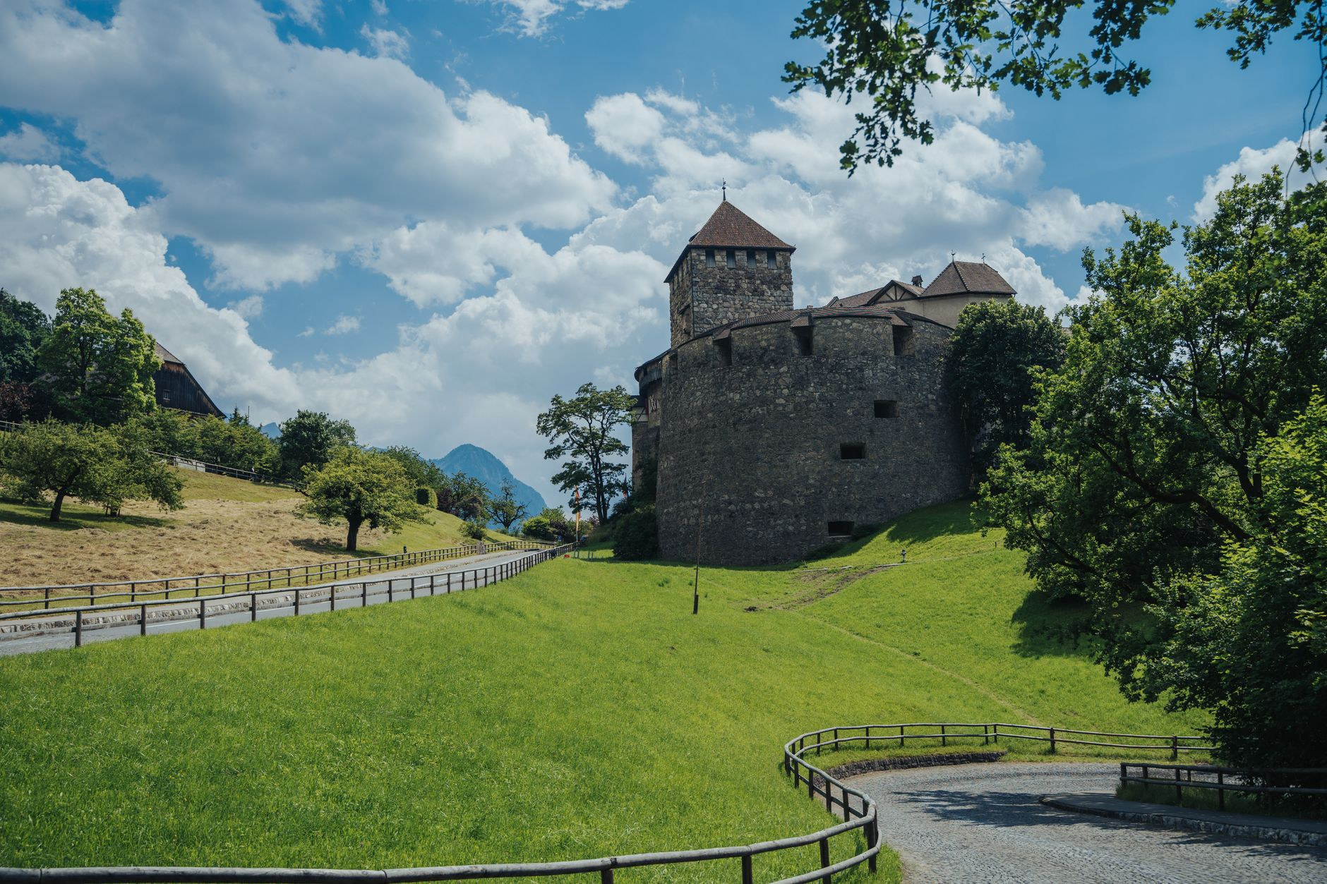 Medieval stone fortress of Vaduz Castle framed by lush green meadows and sloping alpine vineyards