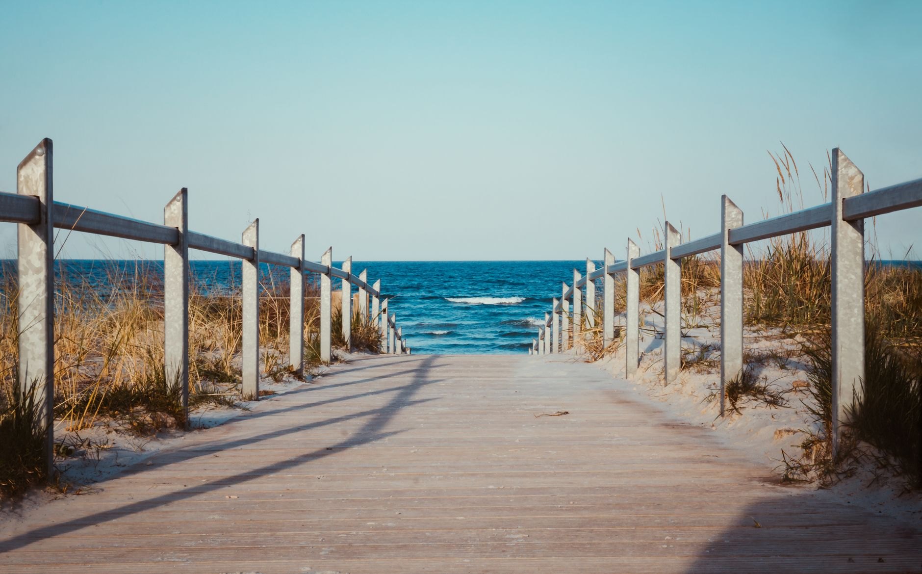 Curving wooden boardwalk running along the crest of massive golden sand dunes overlooking the shimmering Curonian Lagoon