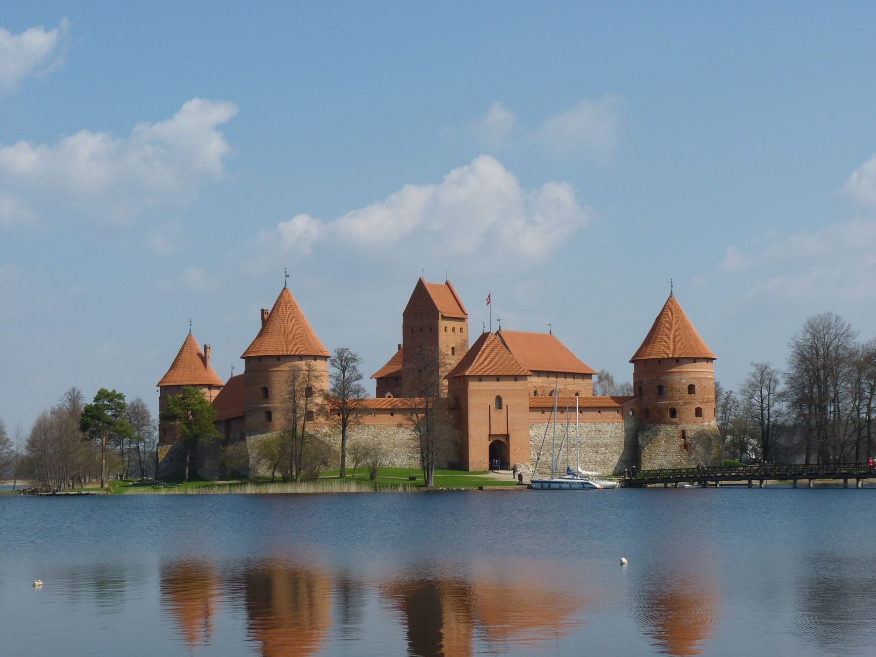 Red-brick fourteenth-century medieval castle standing on an island in Lake Galvė connected by a long wooden pedestrian bridge