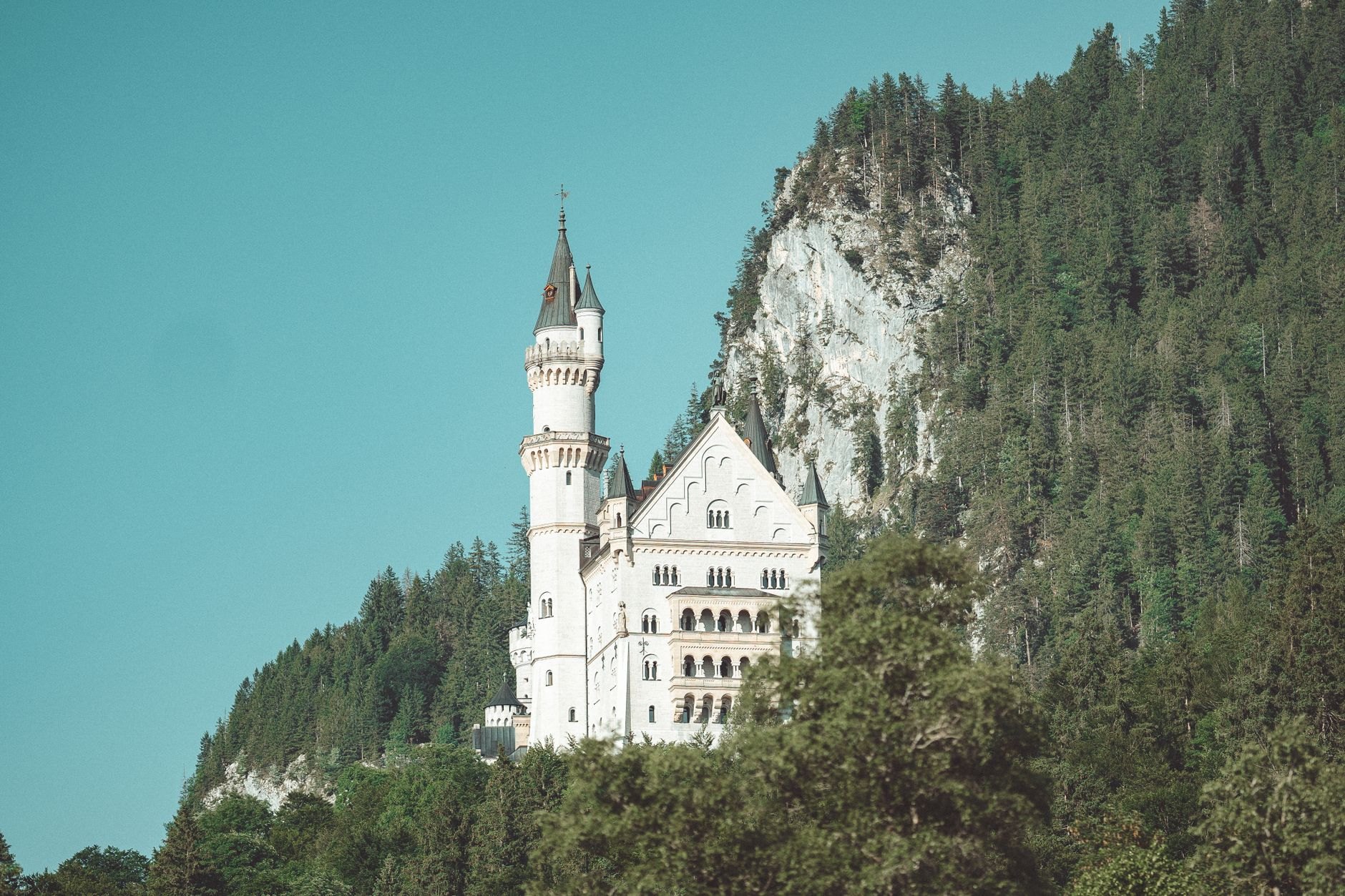 Majestic Romanesque-Gothic medieval stone castle with pointed towers rising high above forested mountain slopes