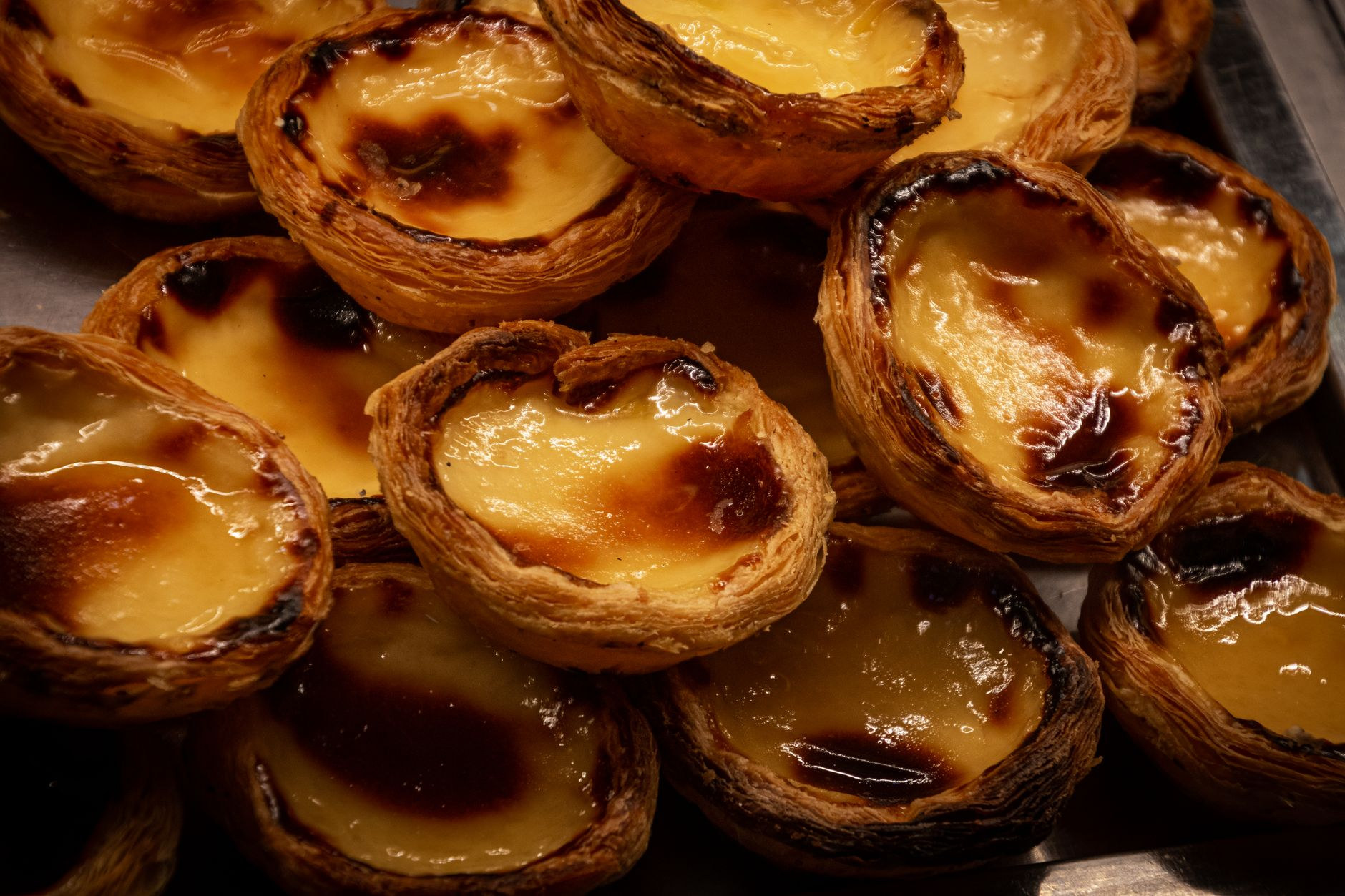 Golden-brown baked Portuguese egg tarts with caramelized custard filling and flaky puff pastry crust displayed fresh from the oven