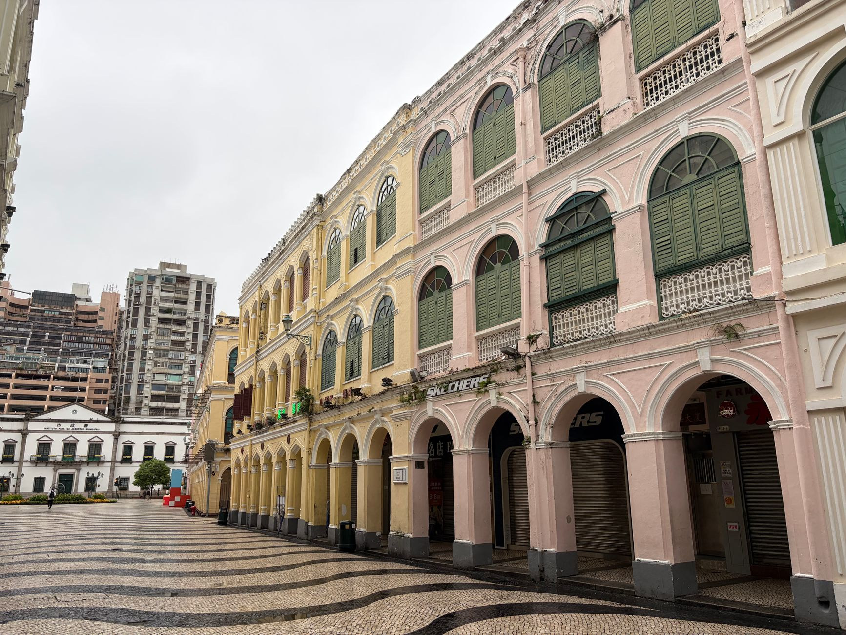 Elegantly restored pastel yellow and green Portuguese colonial architecture with shuttered windows along pedestrian streets in historic Macao