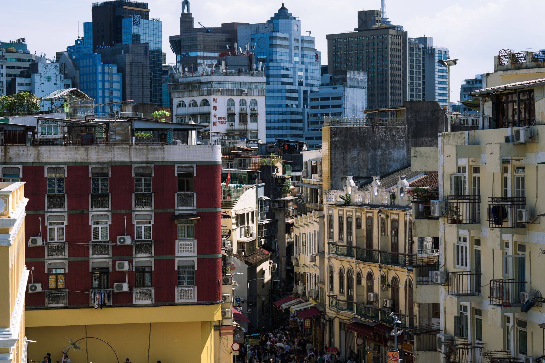 Dramatic perspective looking down a narrow traditional residential street in Macao with a massive futuristic skyscraper rising in the background