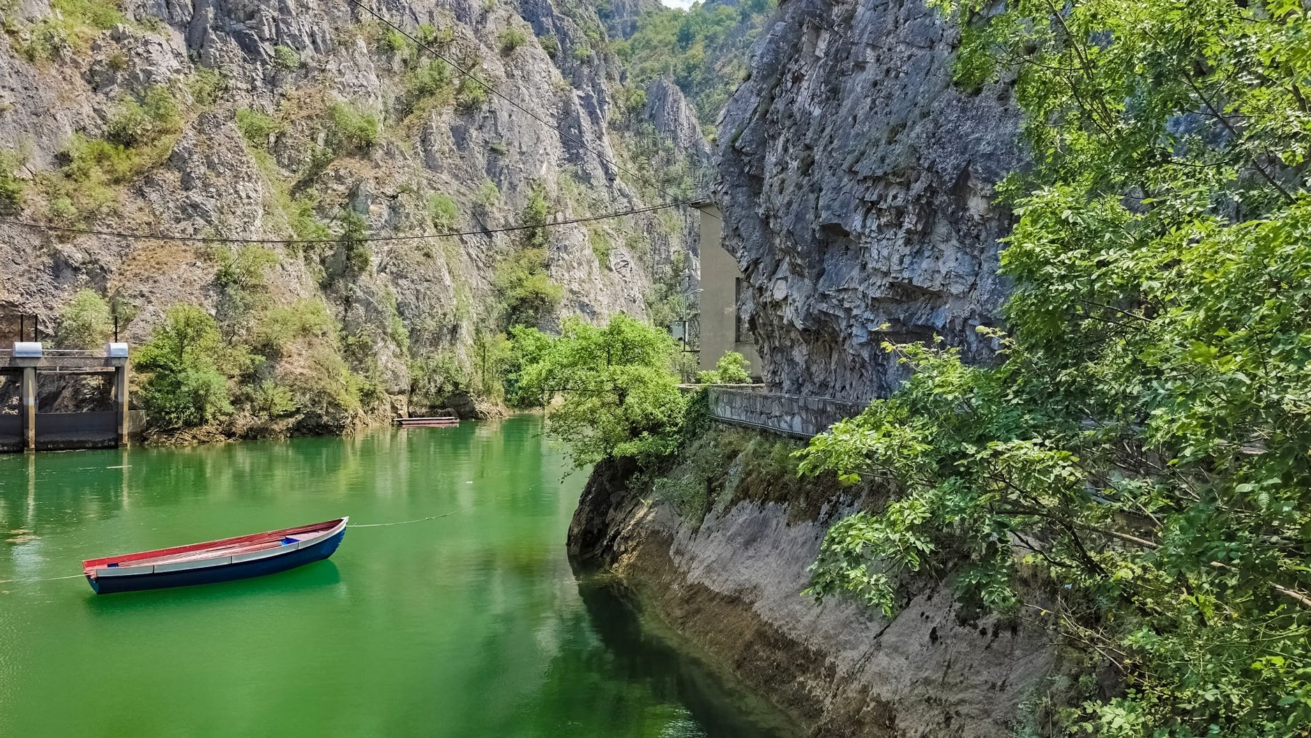 Steep vertical limestone cliffs rising above the emerald-green waters of Matka Canyon with small wooden boats