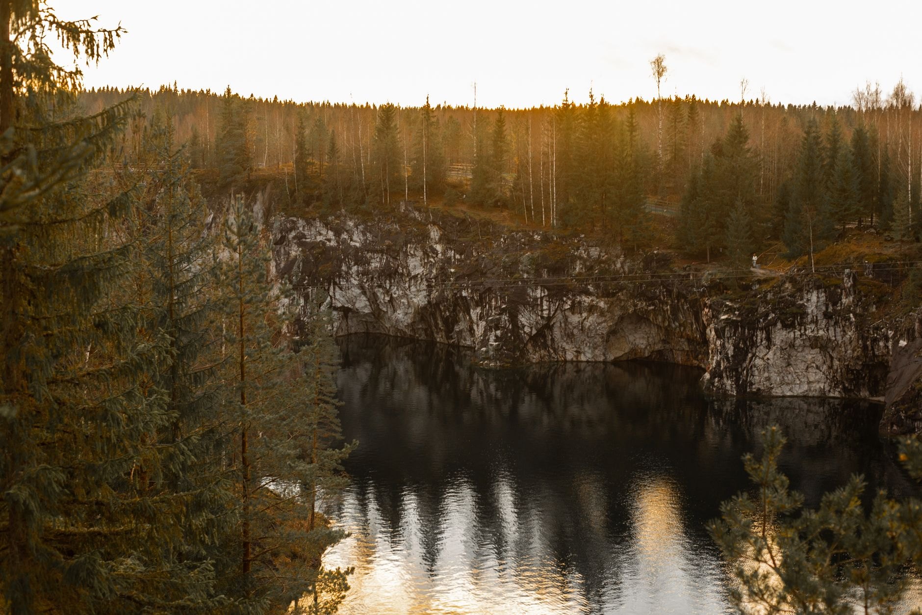 Deep emerald-green volcanic crater lake surrounded by vertical pine-fringed rock cliffs at Lake Tritriva