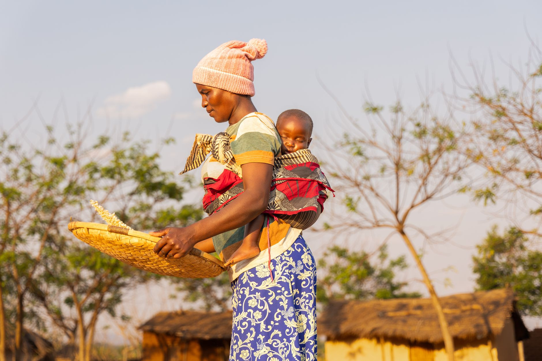 Smiling African mother carrying her baby securely wrapped in colorful fabric in a rural lakeside village in Mangochi