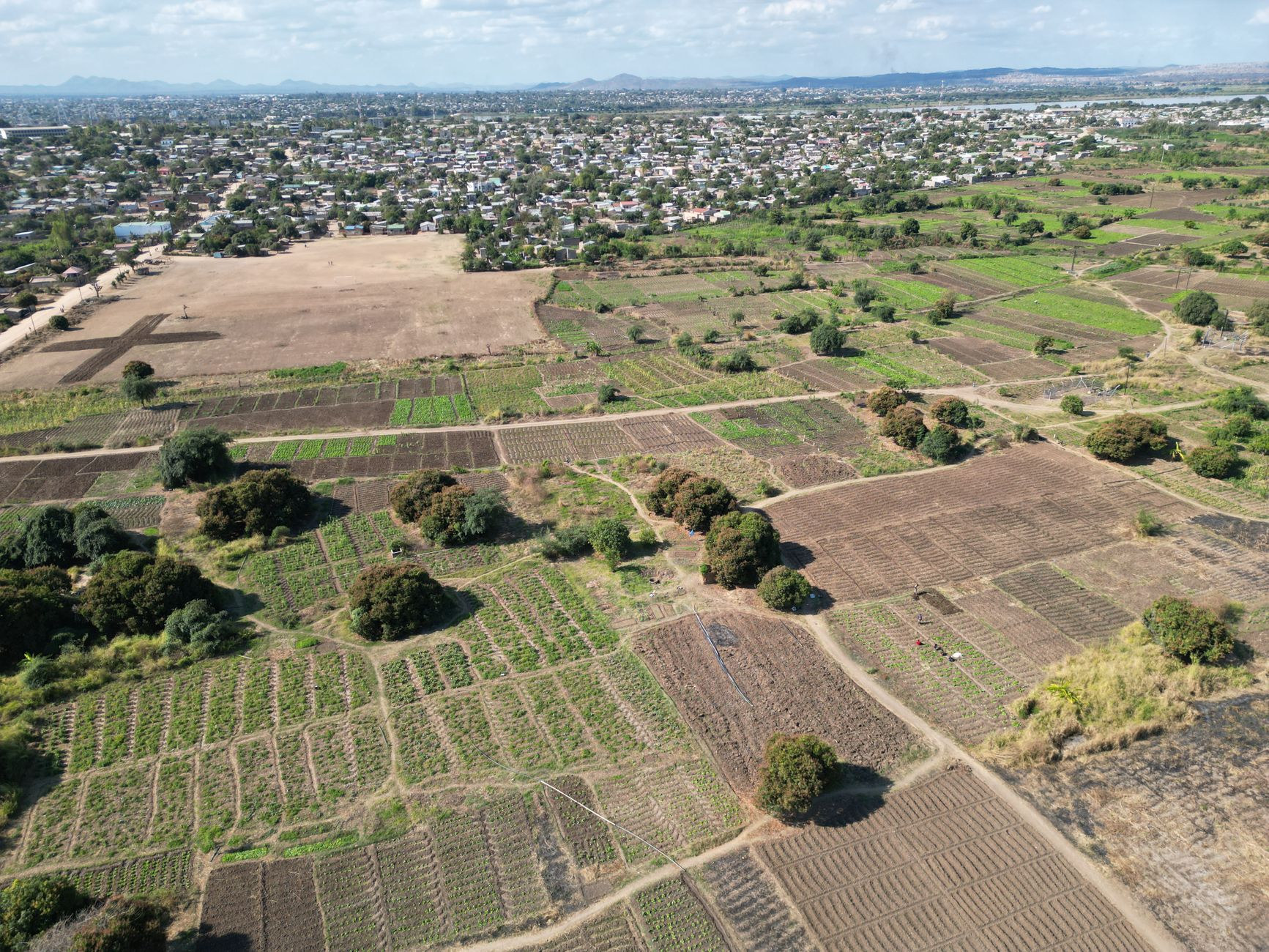 Wide aerial perspective over golden agricultural fields, smallholder farms, and red dirt access roads near Lilongwe